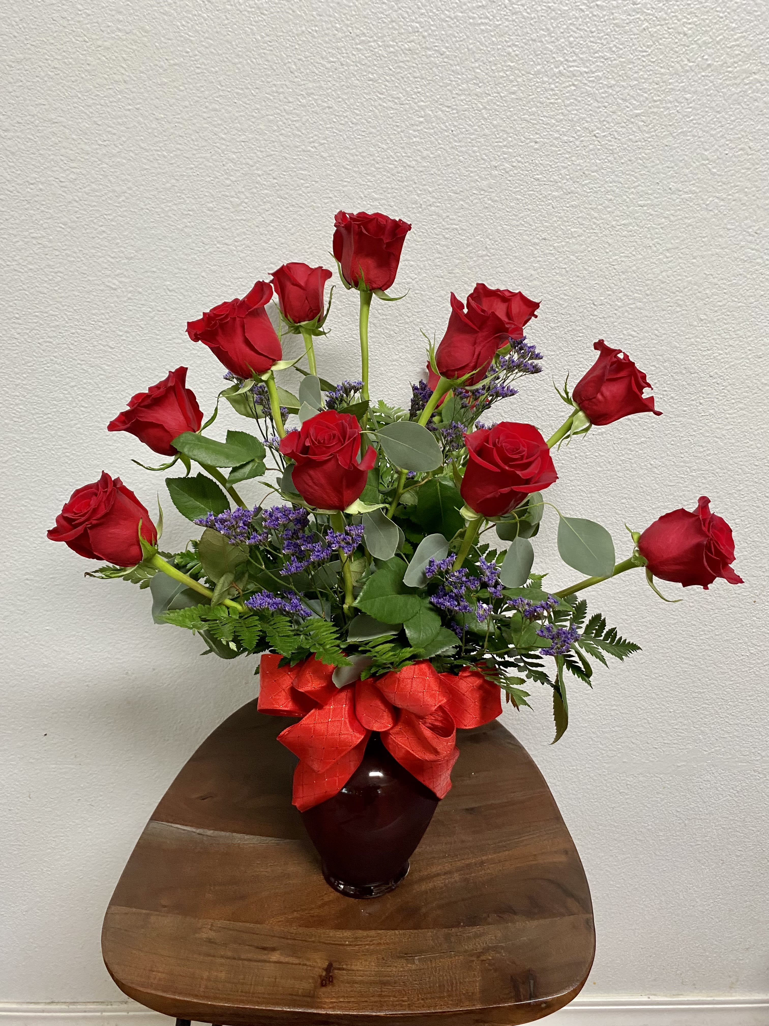 Dozen Red Roses - 12 long stem red roses designed with lush green in red glass vase. Will include white OR purple filler.