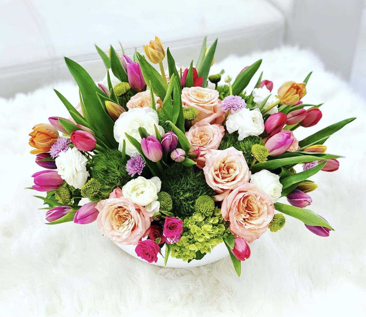 Mixed bouquet of pink, peach, white, and yellow flowers in a white container