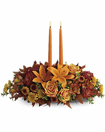 Family Gathering Centerpiece  - As your loved ones gather around the table, they'll bask in the warm glow of two orange taper candles surrounded by a fantastic array of fall flowers.  Orange roses, asiatic lilies, dark orange alstroemeria, bronze button spray chrysanthemums, yellow and rust cushion spray chrysanthemums and fall foliage are exquisitely gathered in this center-of-attention piece.