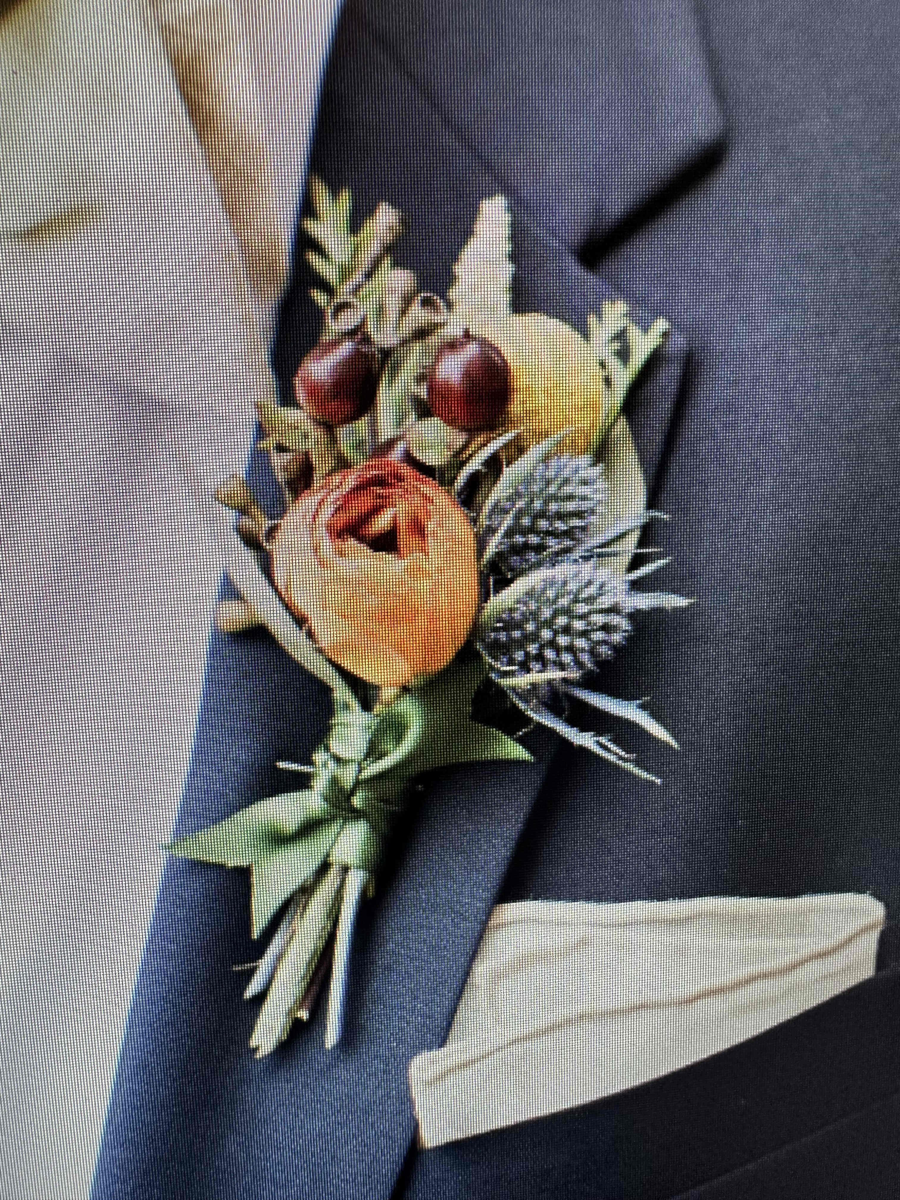 Orange and yellow boutonniere with berries and thistle on a dark suit lapel