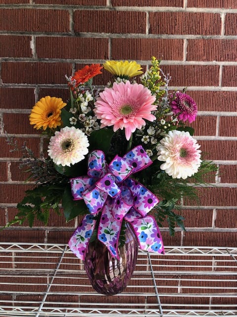 Colorful gerbera daisy arrangement in a purple vase with a patterned bow