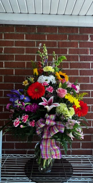 Colorful mixed flower arrangement in a glass vase with a plaid ribbon