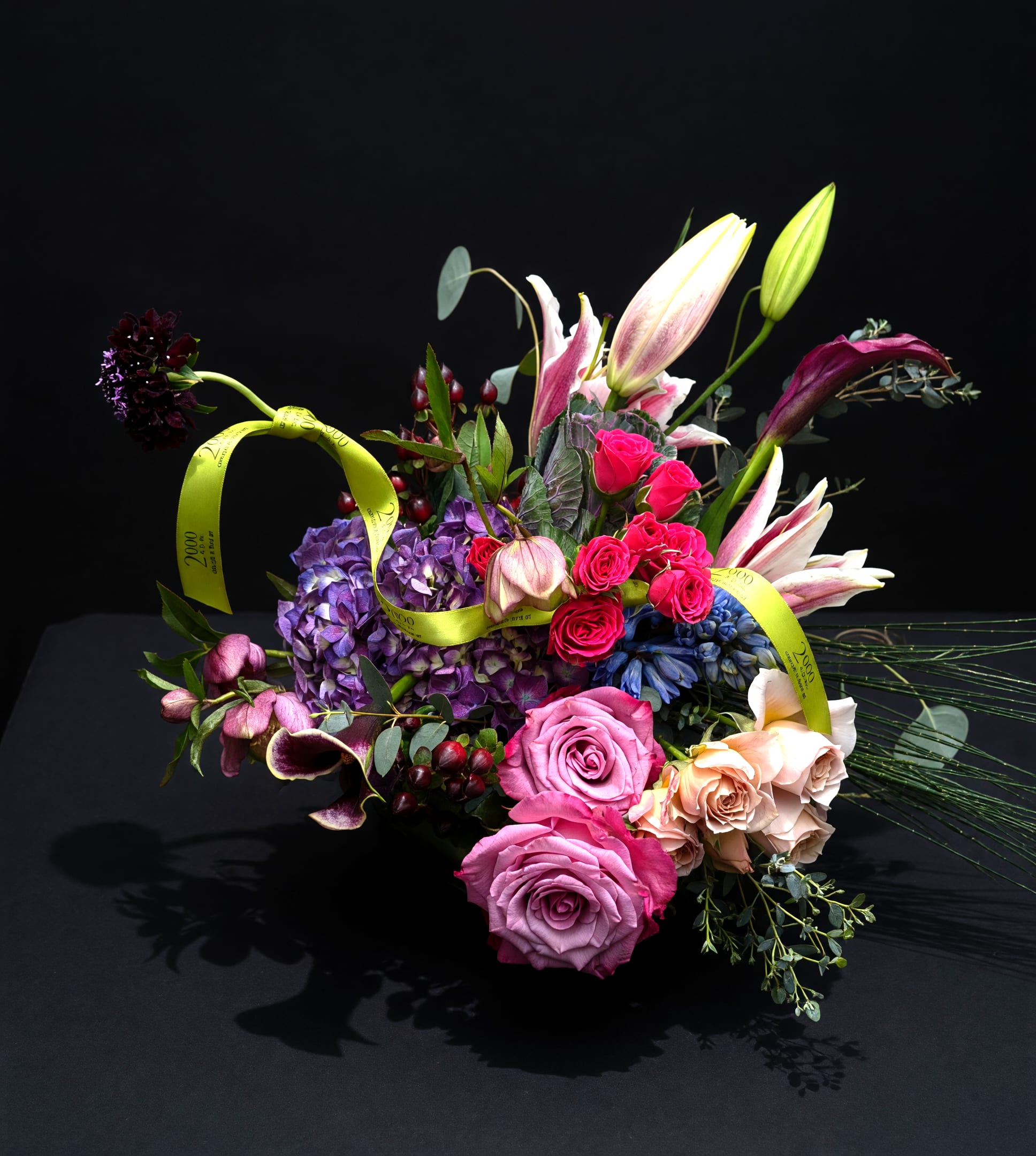 Love Is in the Air - Romantic palette of pinks purples and white with accent foliage. Presented in a clear glass container with exposed stems.