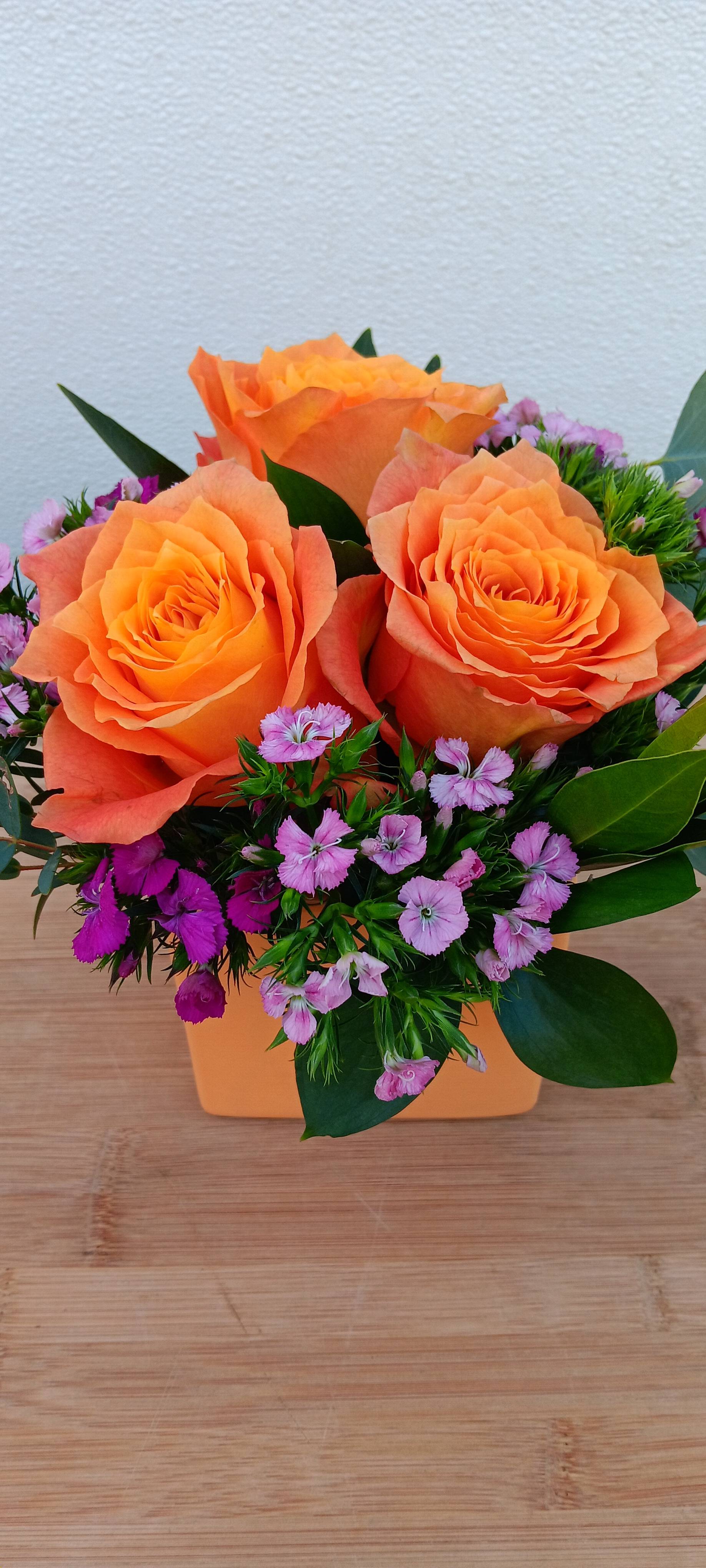 Orange roses with small pink flowers in a square orange vase