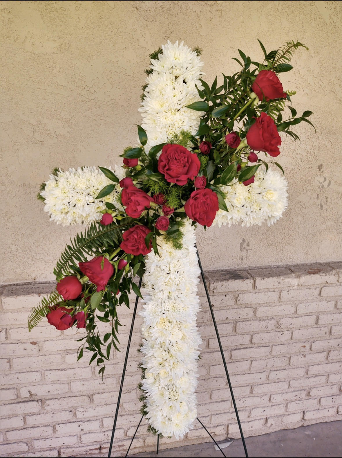 Tall standing white cross arrangement with red roses on a metal easel