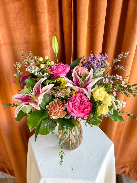 Bouquet of pink lilies, roses, and yellow blooms in a glass vase