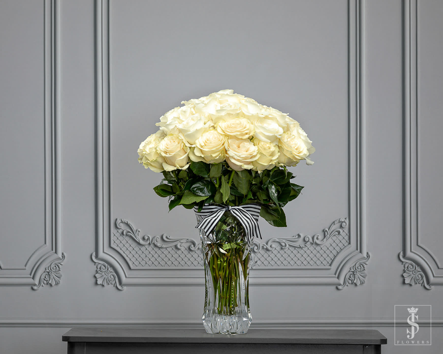 Cream rose bouquet in a clear glass vase with a striped ribbon
