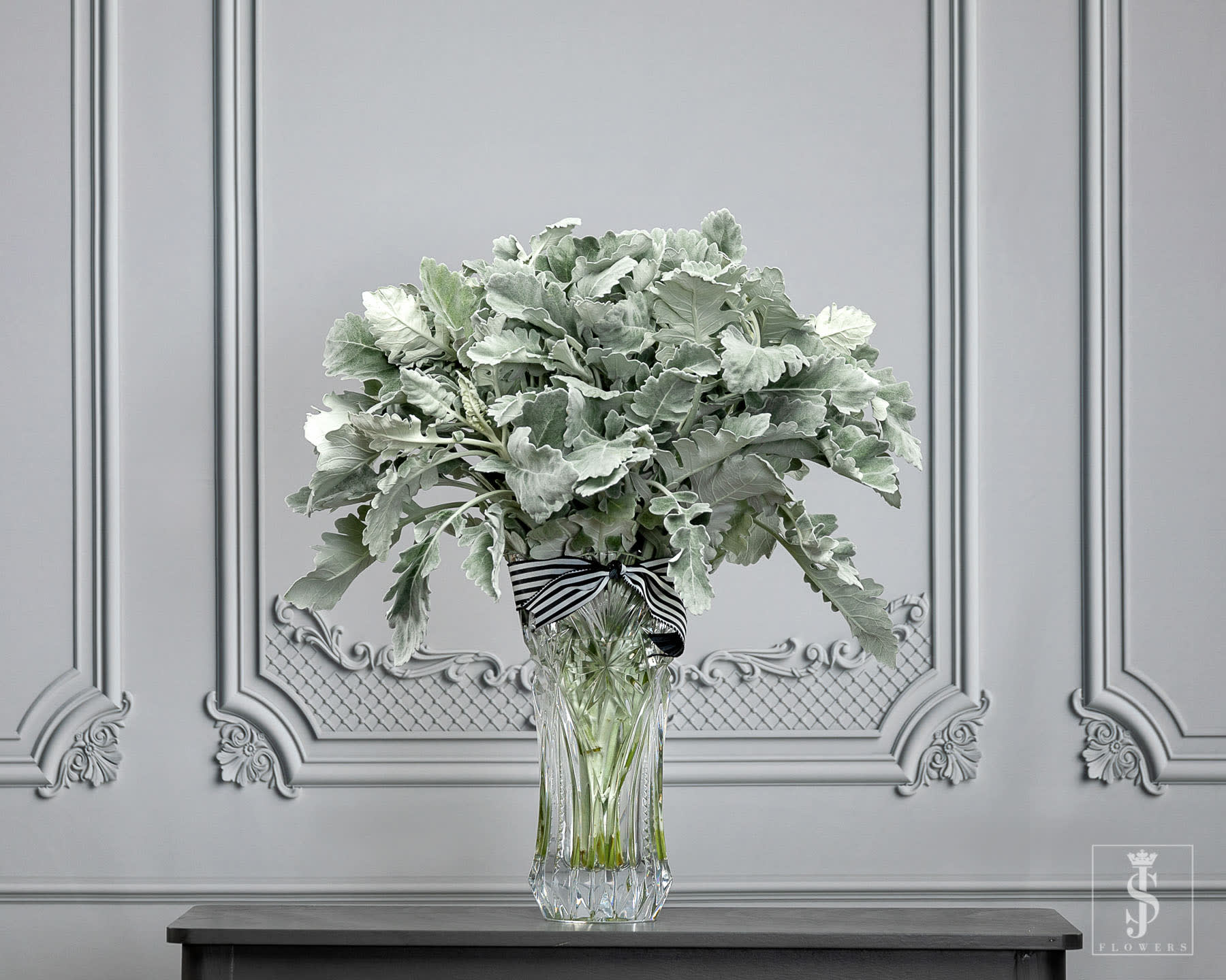 Silvery-green foliage arrangement in a clear glass vase with a striped ribbon