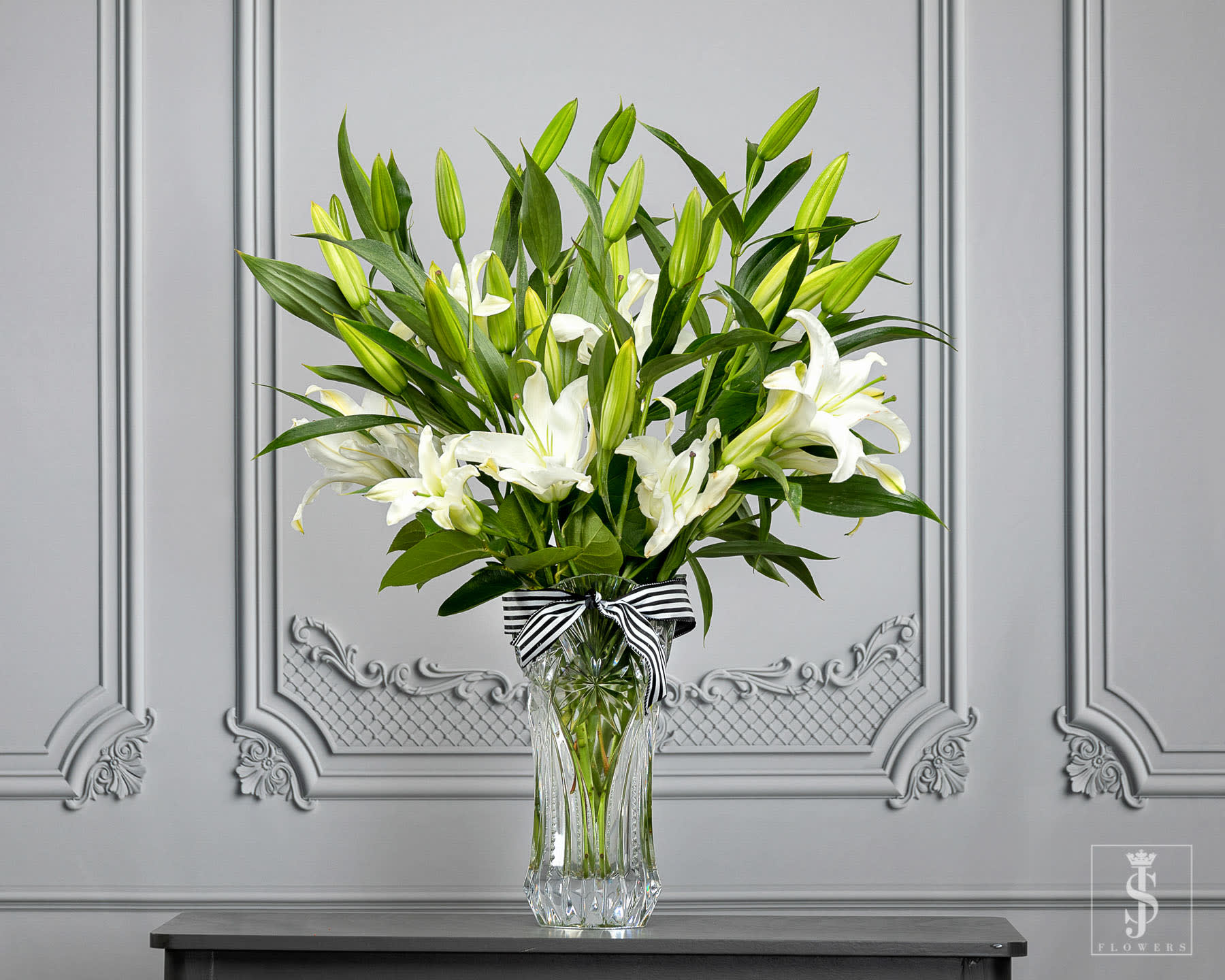 White lilies in a clear glass vase with a striped ribbon