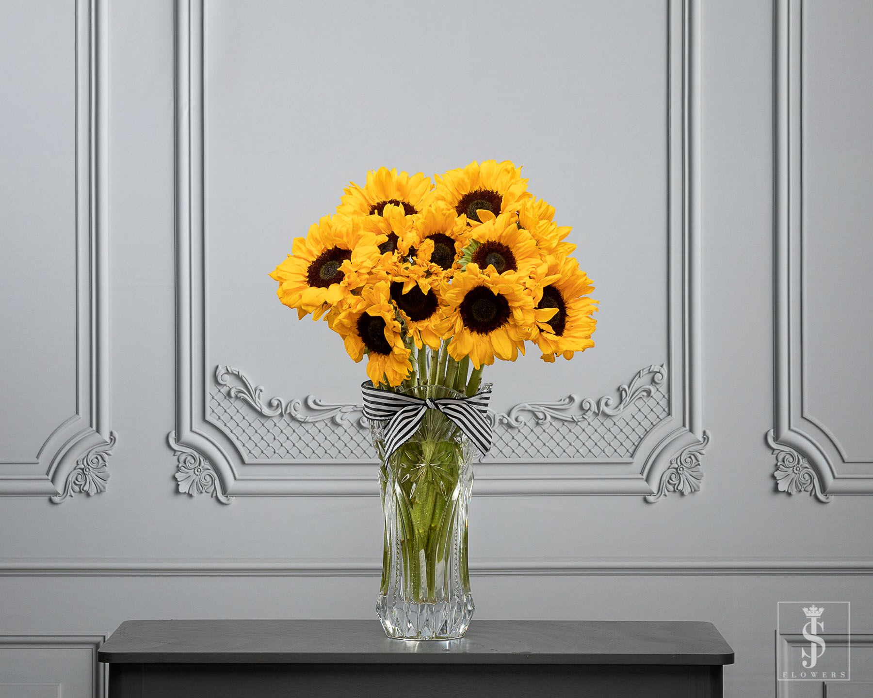 Bouquet of yellow sunflowers in a clear glass vase with a striped ribbon