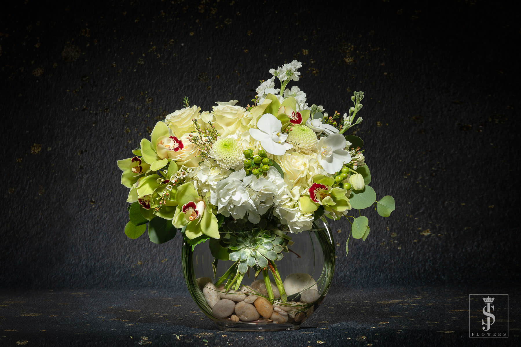 White and pale green floral arrangement in a round glass vase with stones