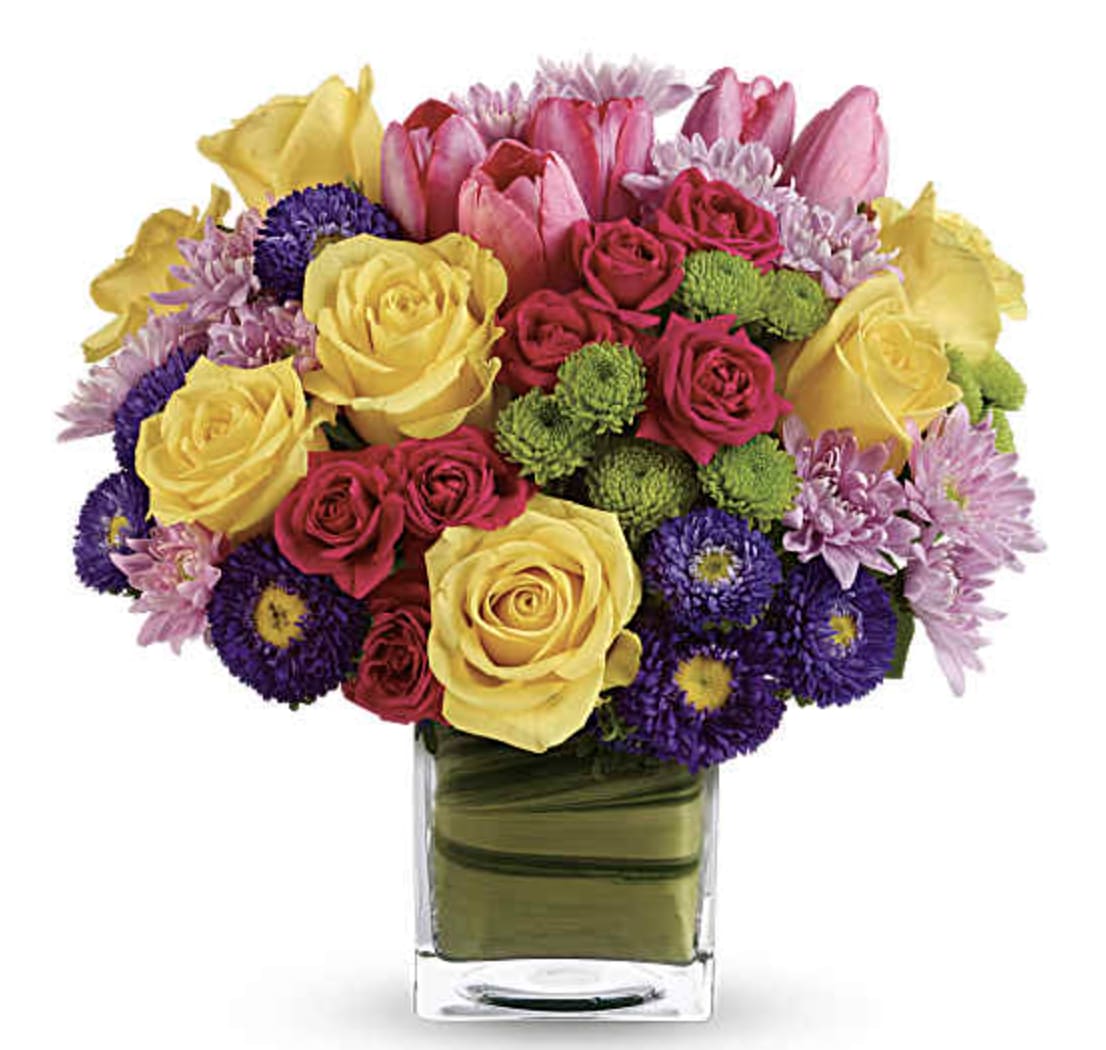Blossom Arrangement - A chic, stylish twist on classic spring flowers! Creamy yellow roses pop against the bright pastel flowers of this modern arrangement, presented in a glass cube vase that's lined with a tropical aspidistra leaf. A high-fashion pick for the haute Couture set! Light yellow roses and carnations are contrasted with bright blooms including hot pink roses, hot pink tulips, purple matsumoto asters, green button mums and lavender cushion spray mums. An aspidistra leaf lines the inside of its modern cube vase. Orientation: All-Around
