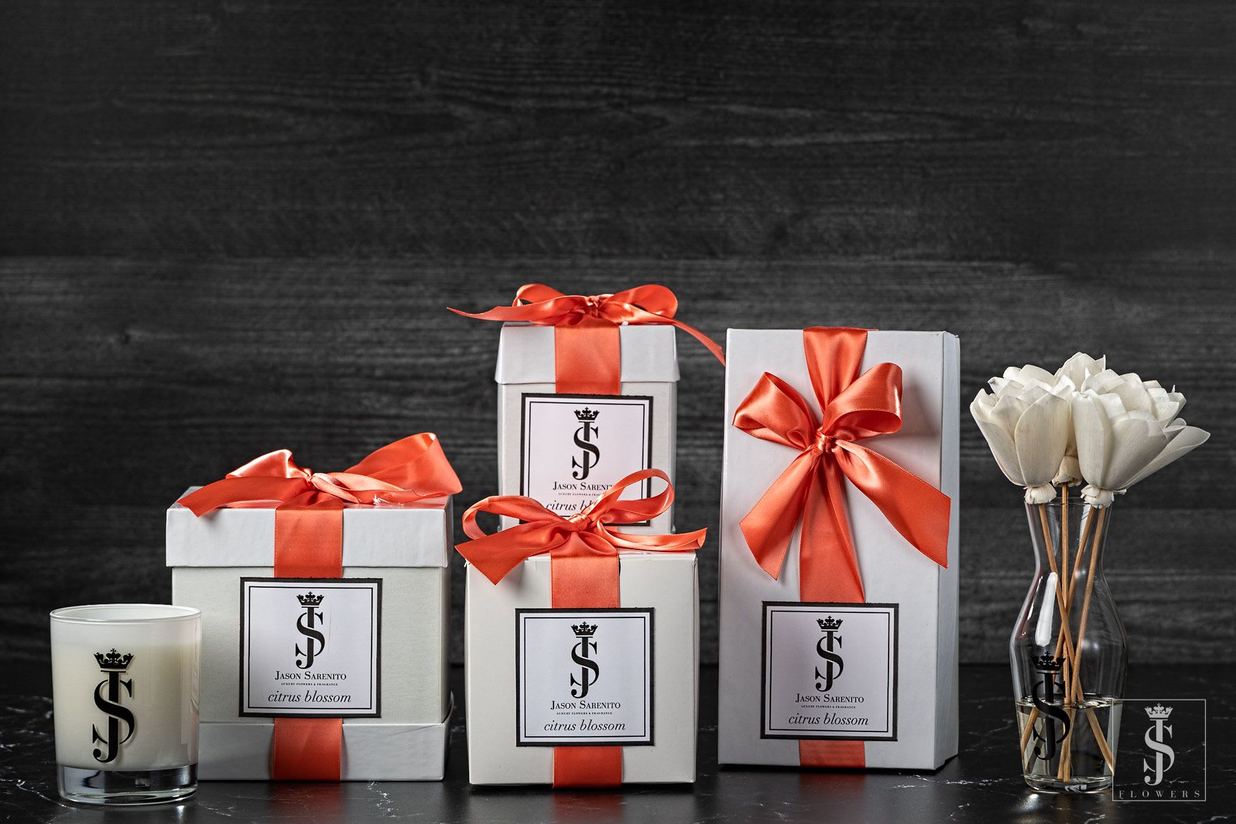 Gift boxes with orange ribbons beside a candle and white flowers in a vase