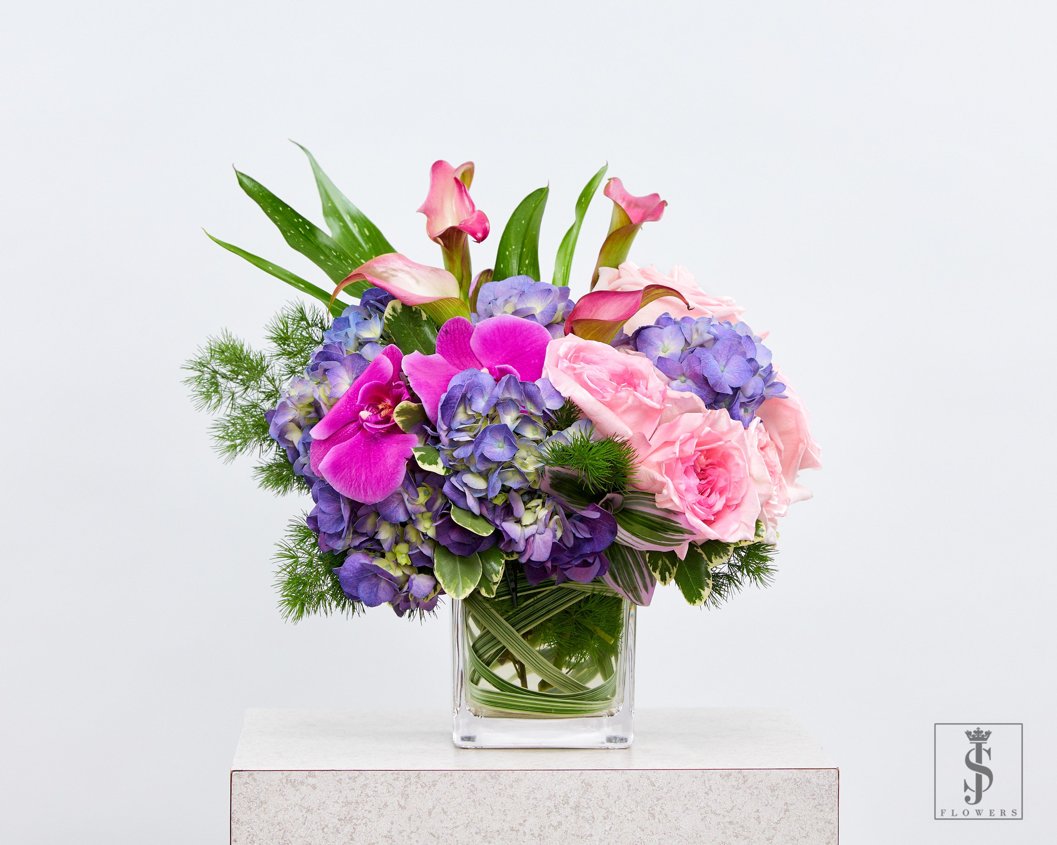 Pink orchids and roses with purple hydrangeas in a clear glass vase