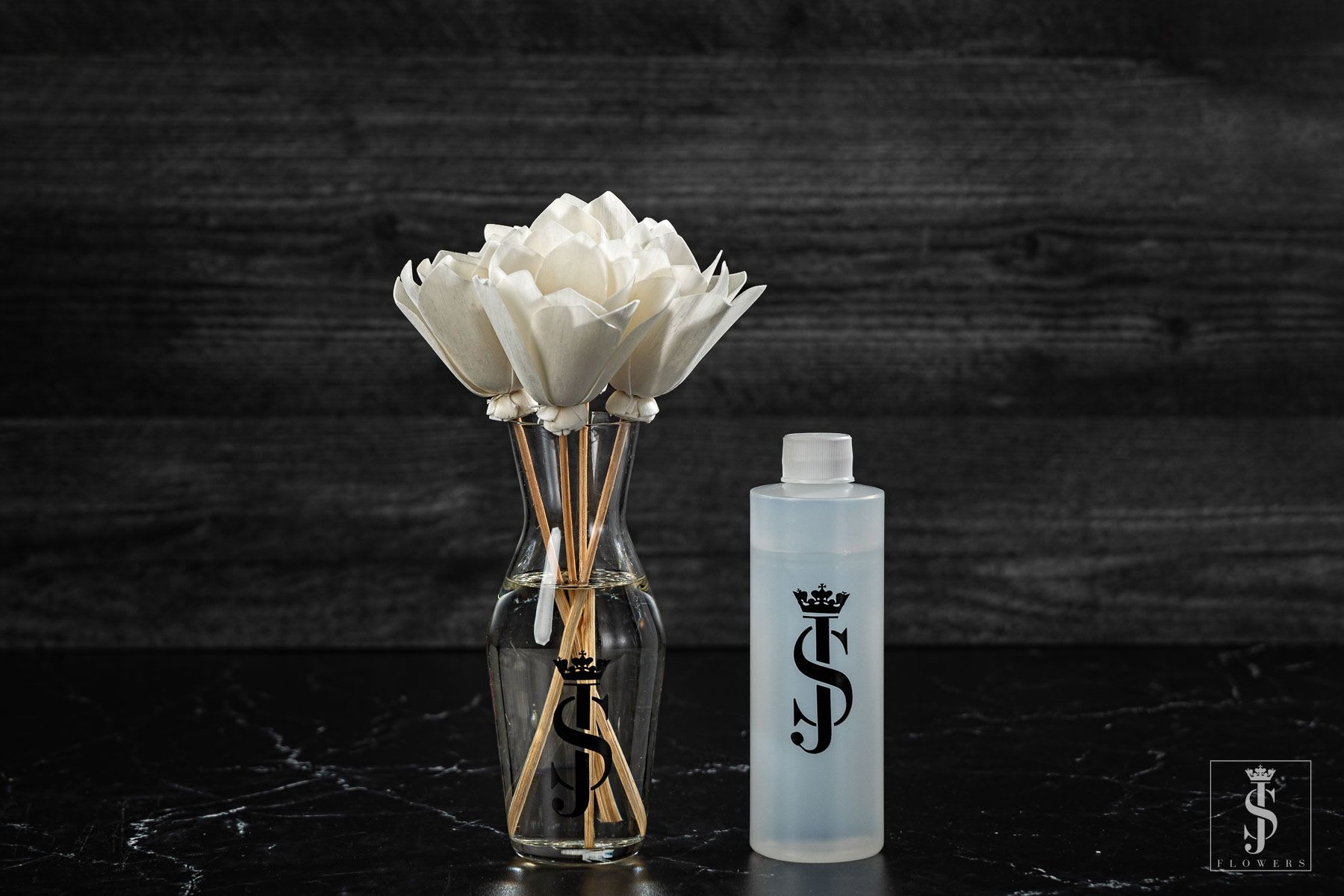 White artificial flowers in a clear glass vase beside a frosted bottle