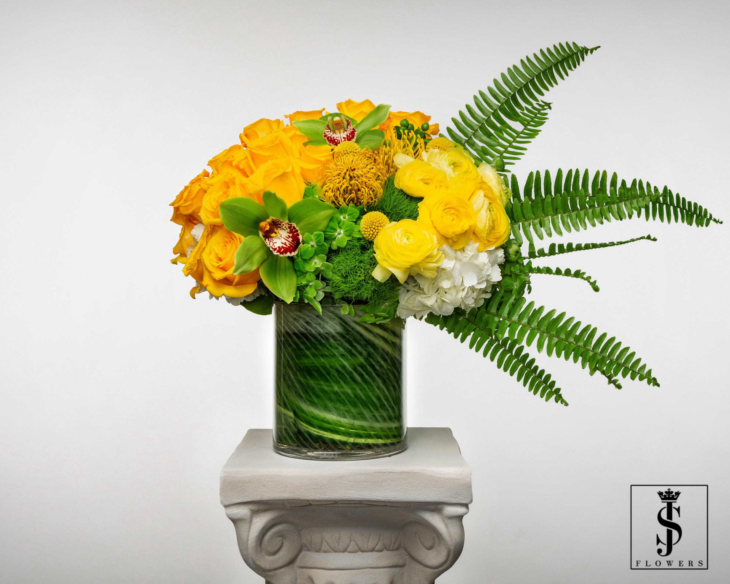 Yellow floral arrangement in a glass vase with fern fronds