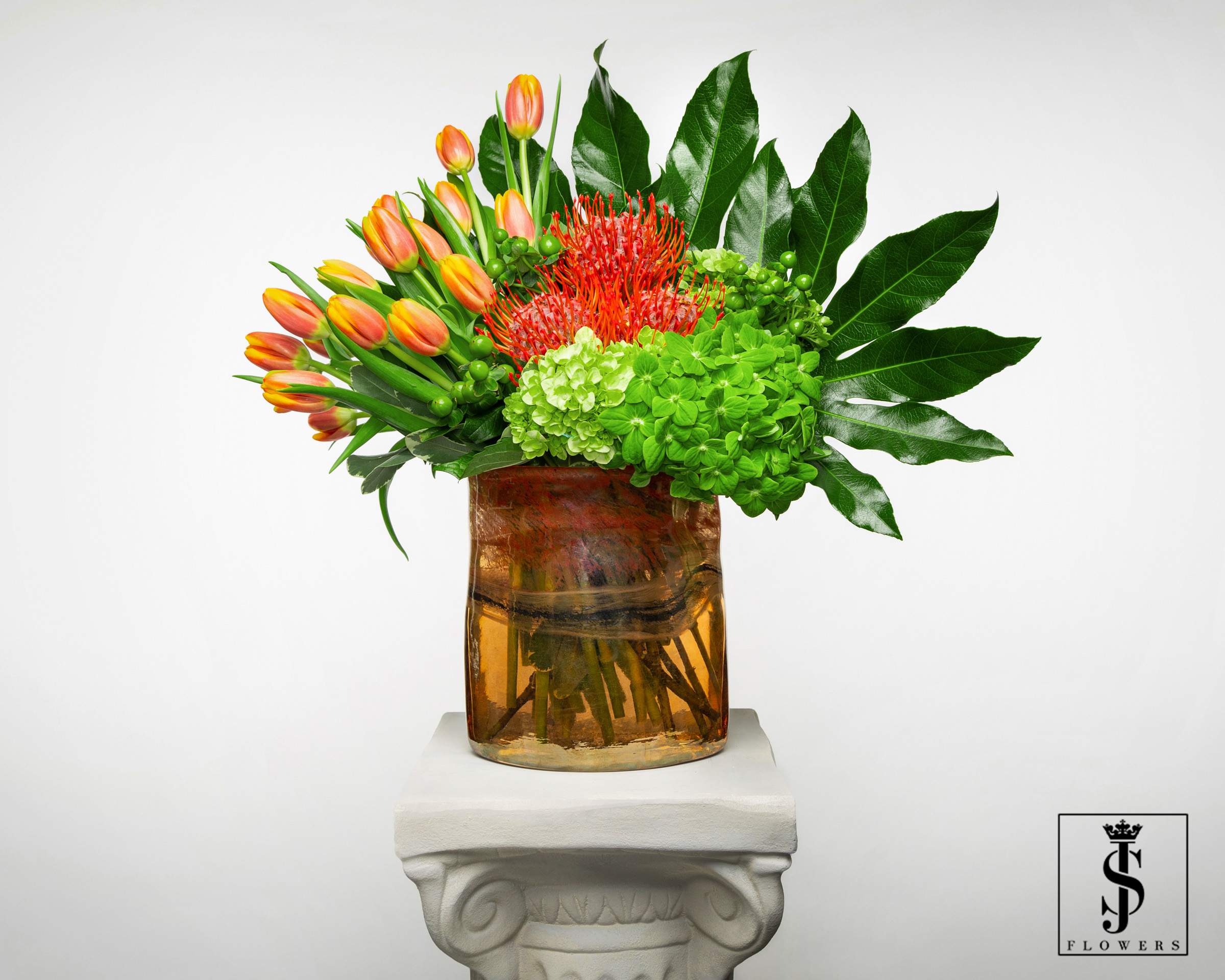 Orange tulips and red tropical flowers in an amber glass vase