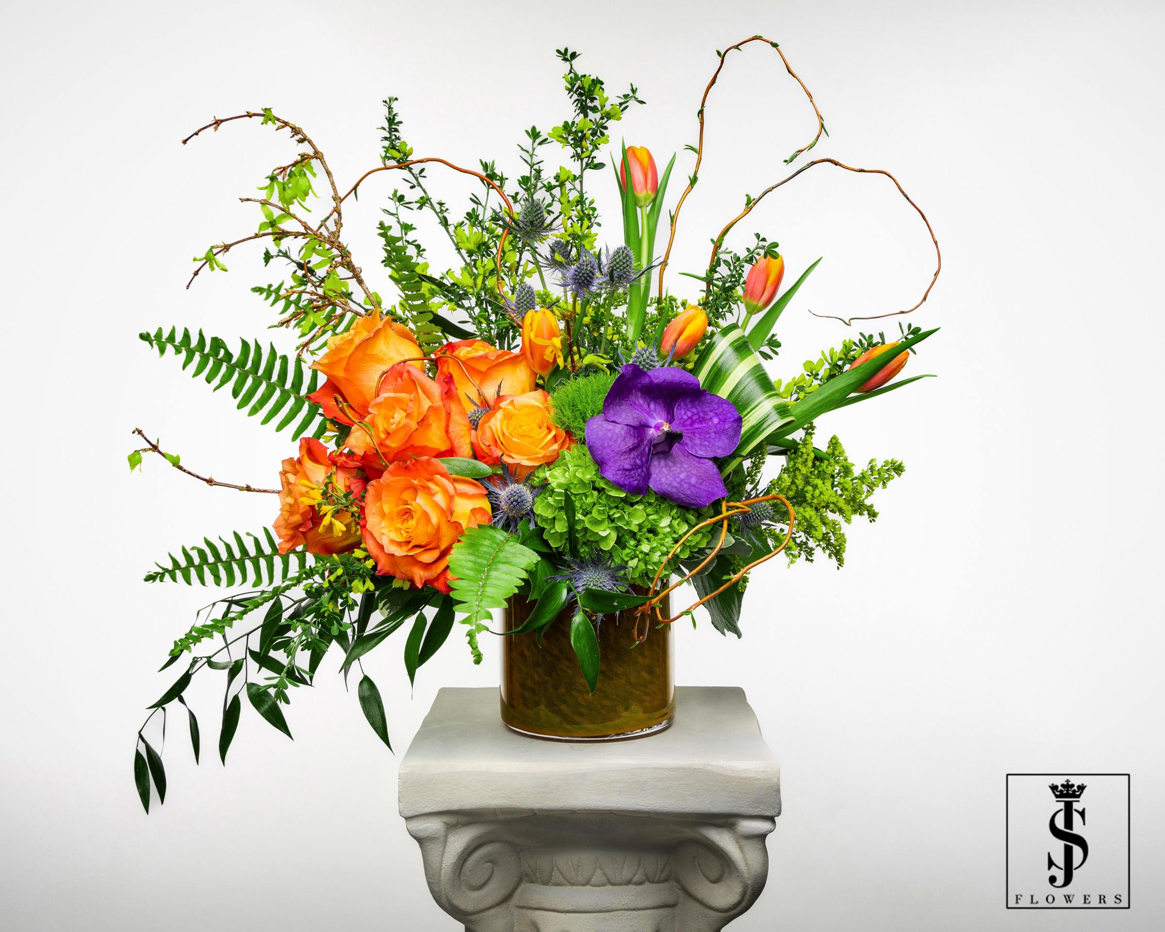 Orange roses and tulips with a purple orchid in a glass vase