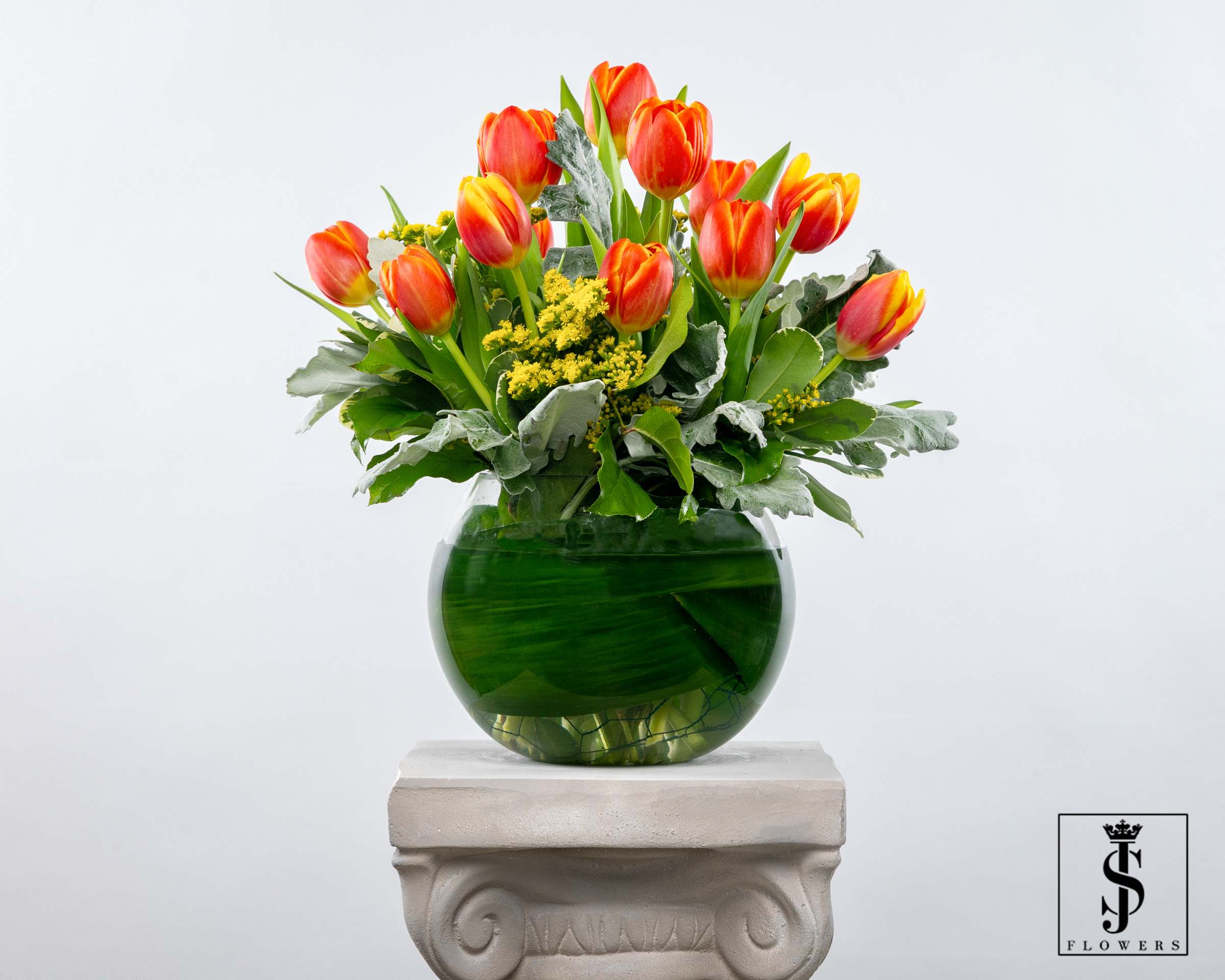 Orange and yellow tulips in a green glass vase