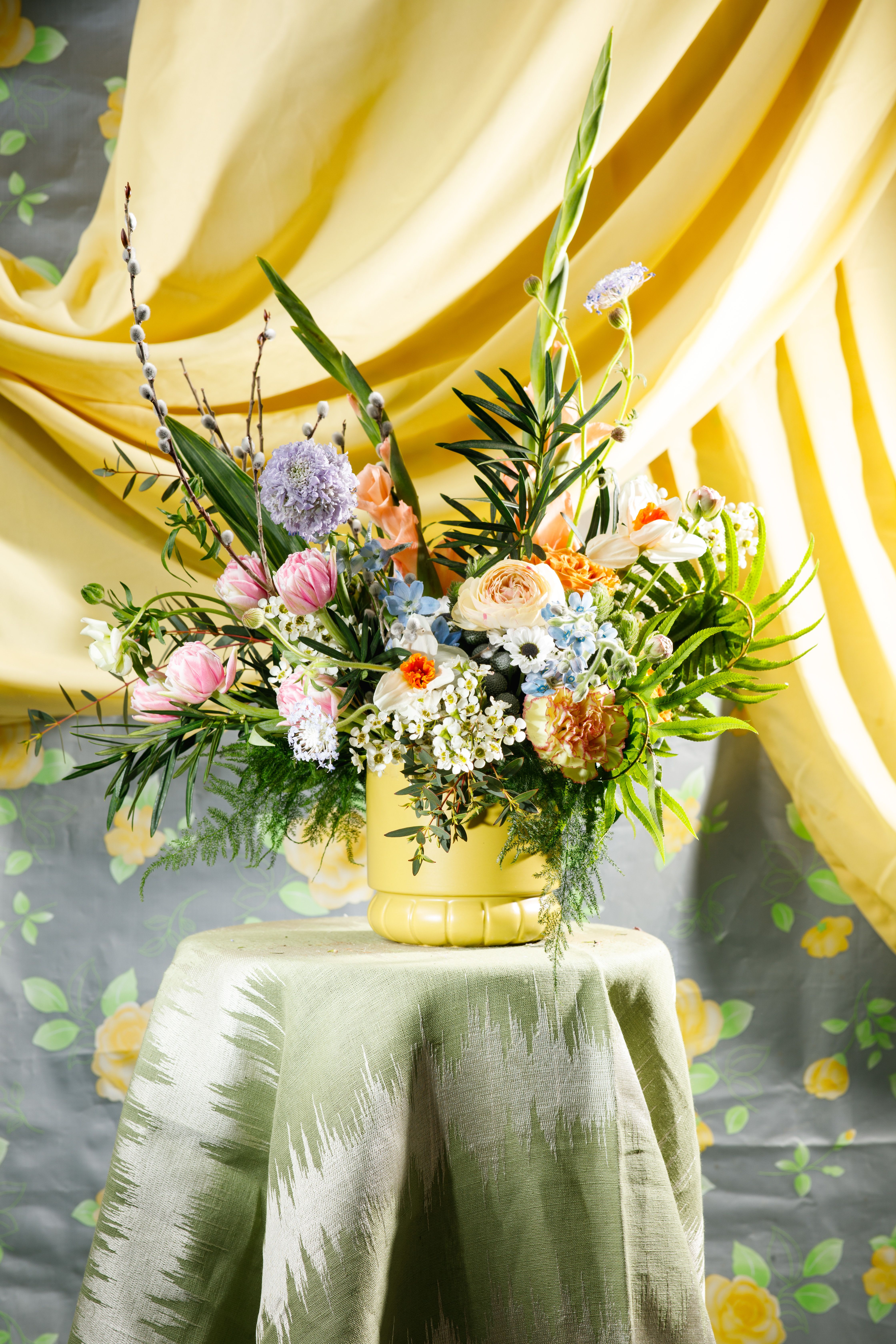 Colorful mixed flower arrangement in a yellow vase on a draped table