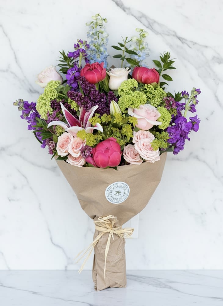 Spring Favorites Wrapped Bouquet - Wrapped bouquet to include a selection of all the best spring has to offer. We will choose from our selection of ranunculus, tulips, lilac, verburnum, roses, lilies, and peonies and more.  Exact design and color scheme may vary.