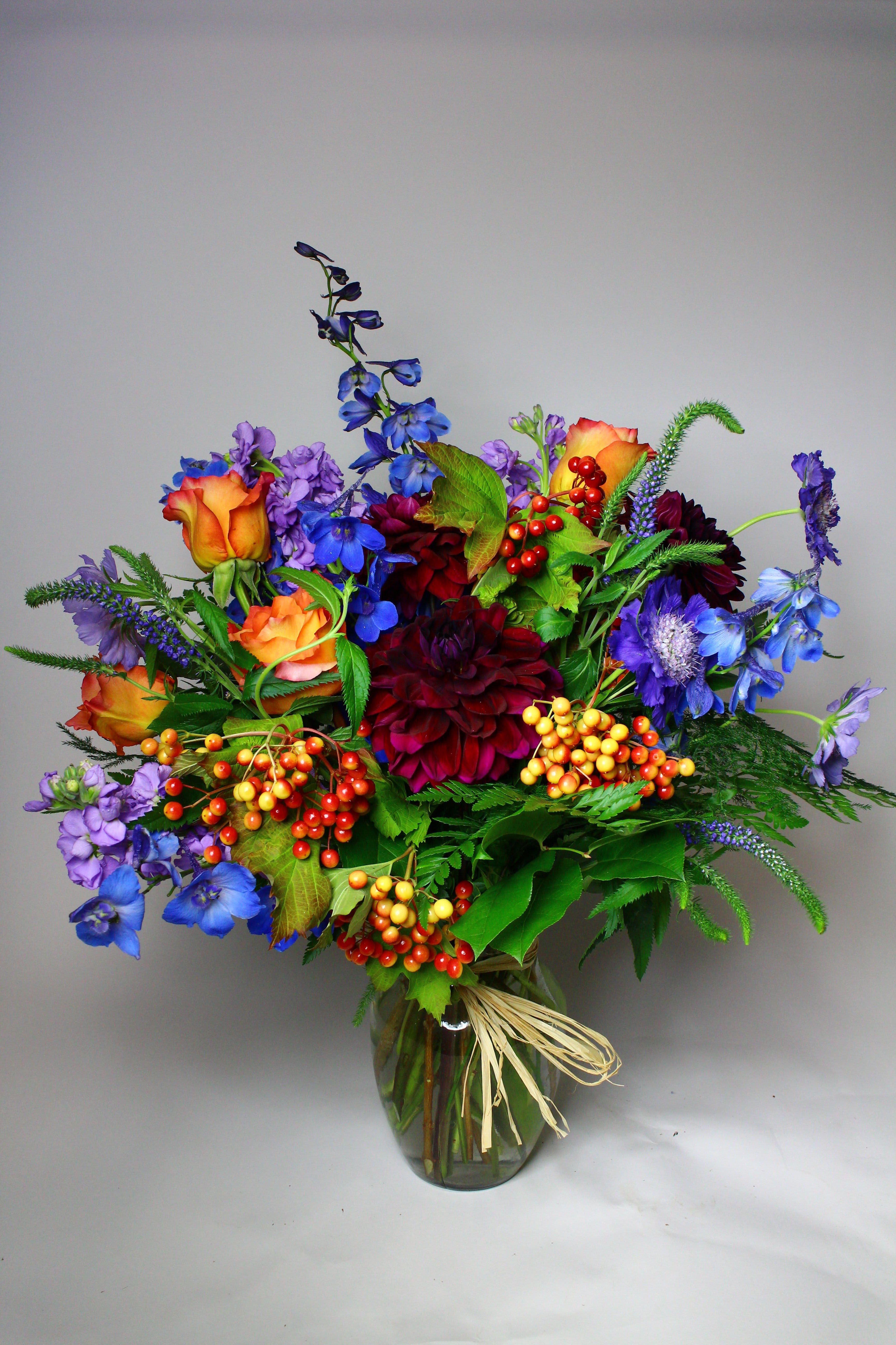 Colorful mixed bouquet in a glass vase with orange roses and blue flowers
