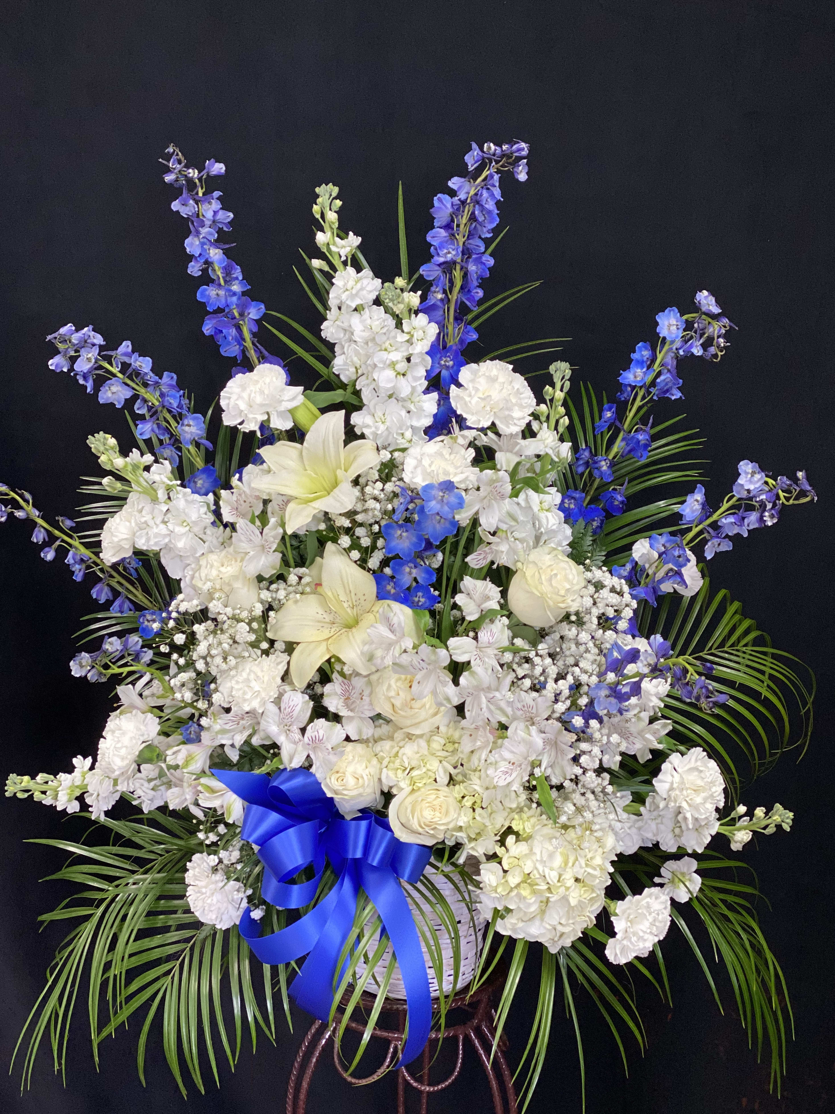 In Loving Memory - Express your sincerest sympathies with  soothing blue delphiniums white roses, lilies and more are with fresh greenery. It’s a comforting gesture that will honor a life so beautifully lived.