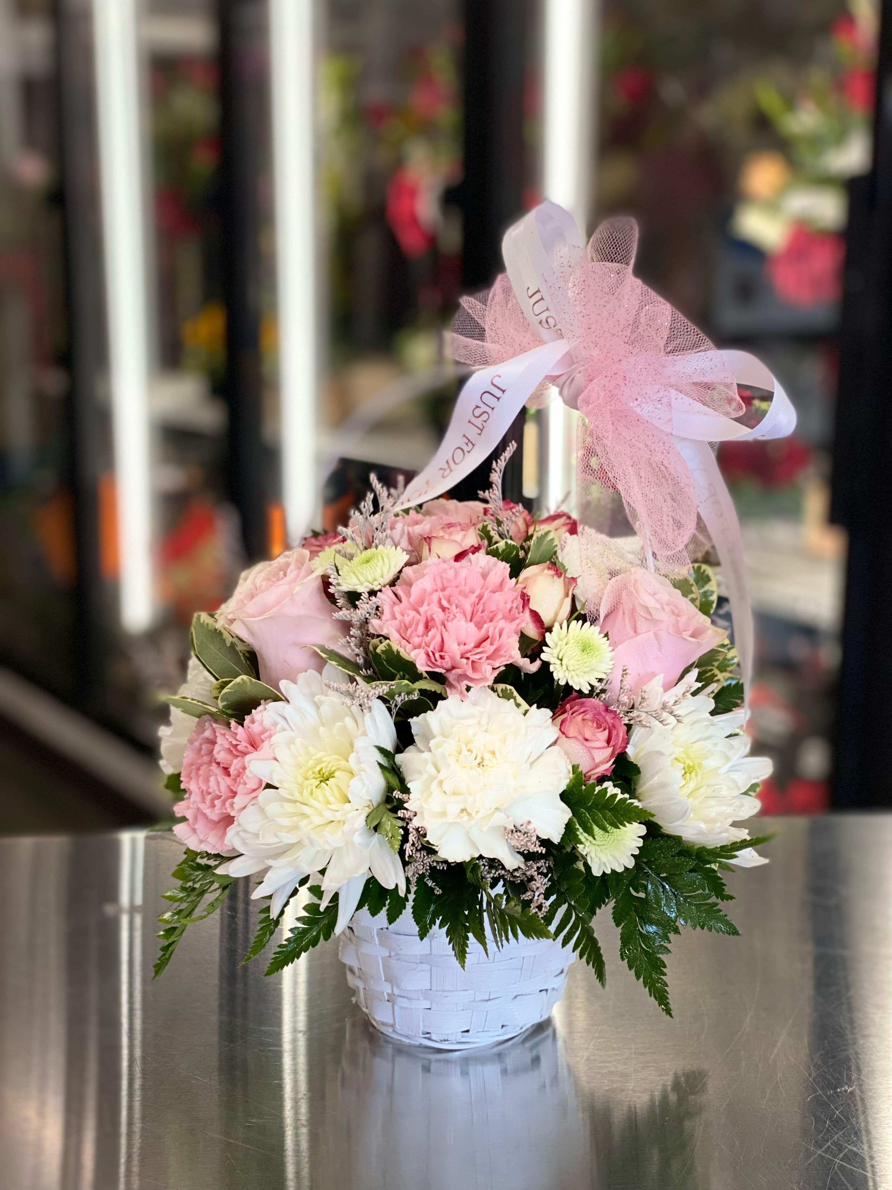 Pink and white flowers arranged in a white basket with a pink ribbon