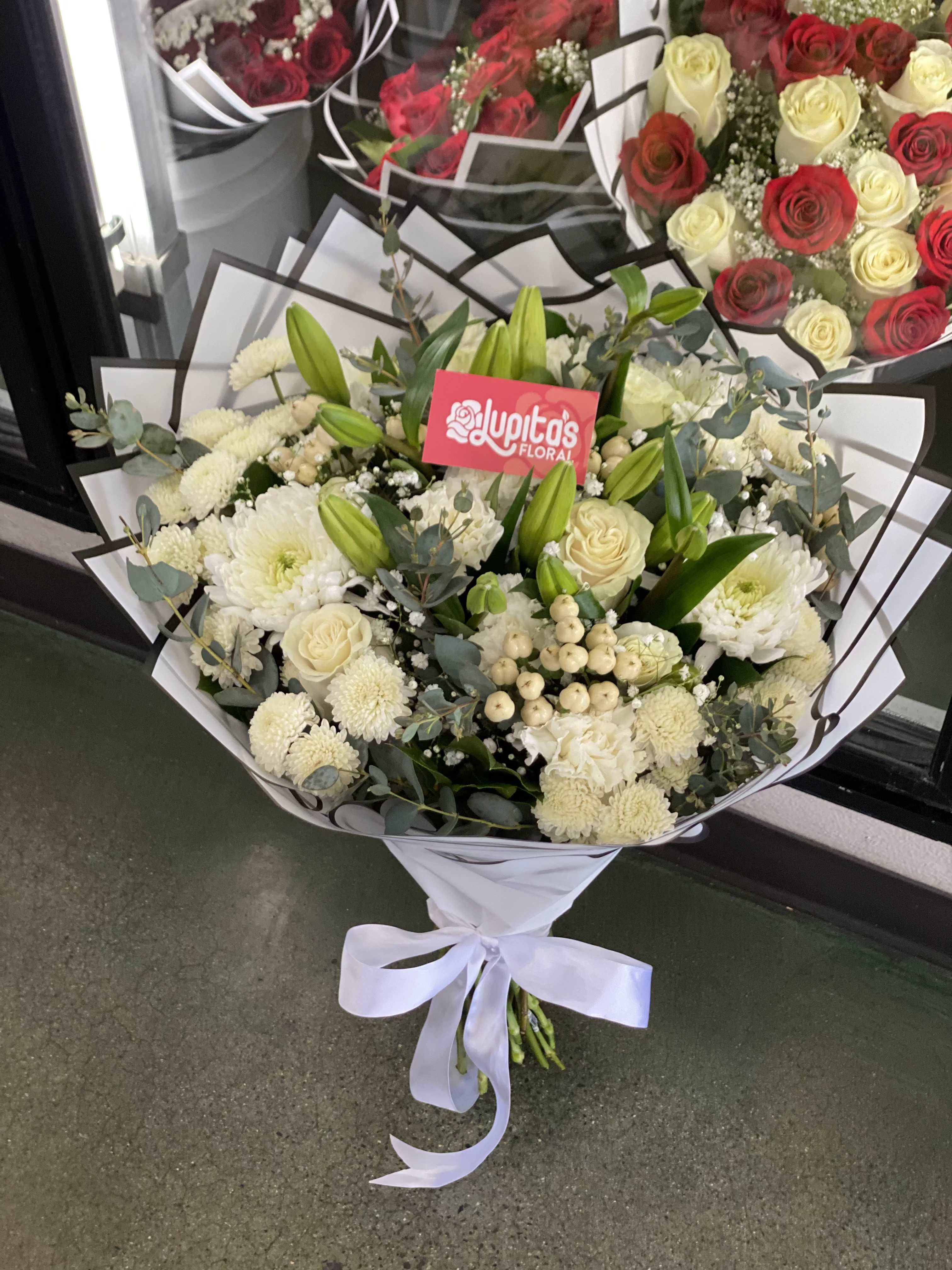 White bouquet with roses, chrysanthemums, and lilies wrapped in paper