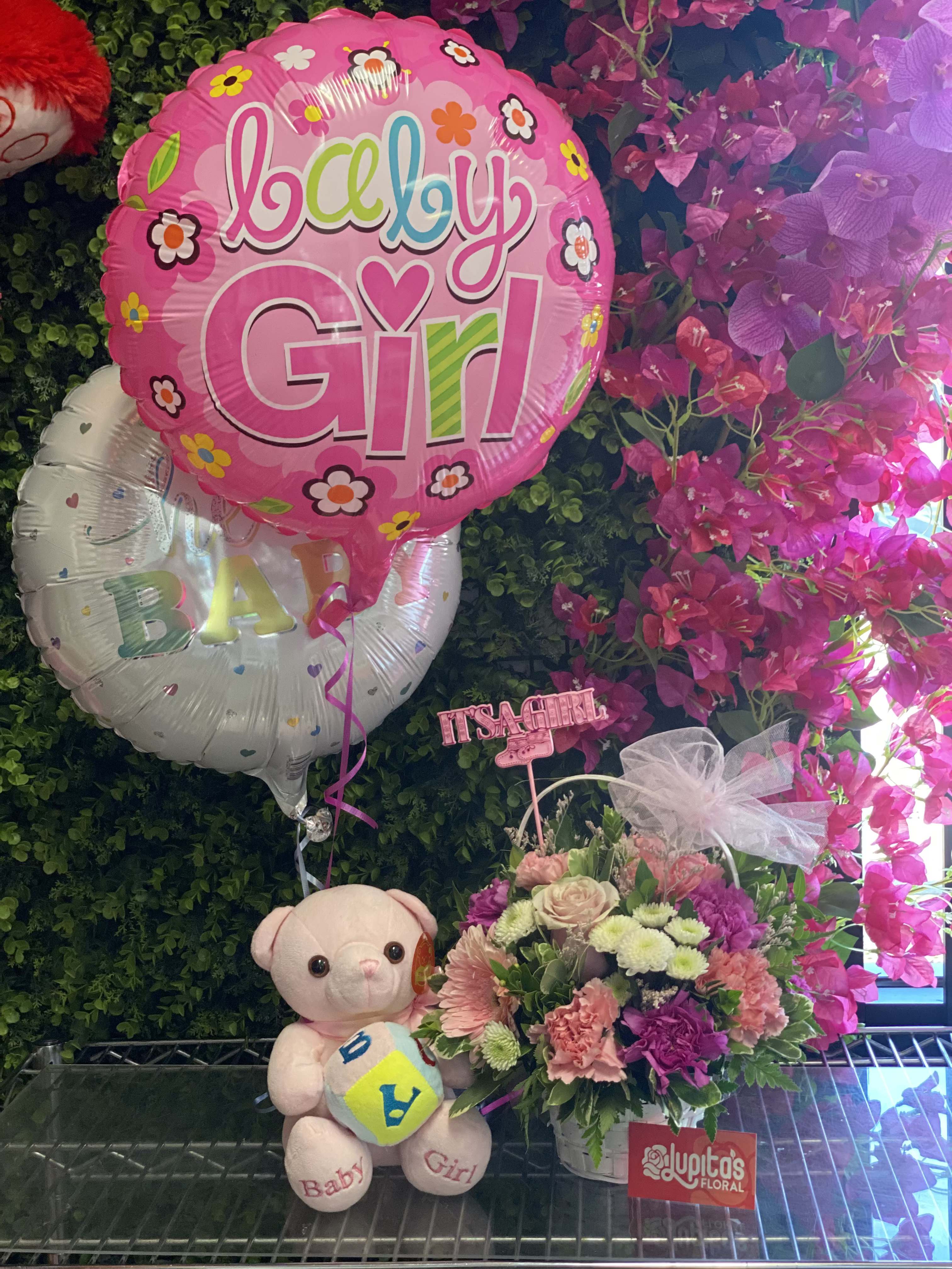 Pink baby girl balloon with flowers, teddy bear, and floral arrangement