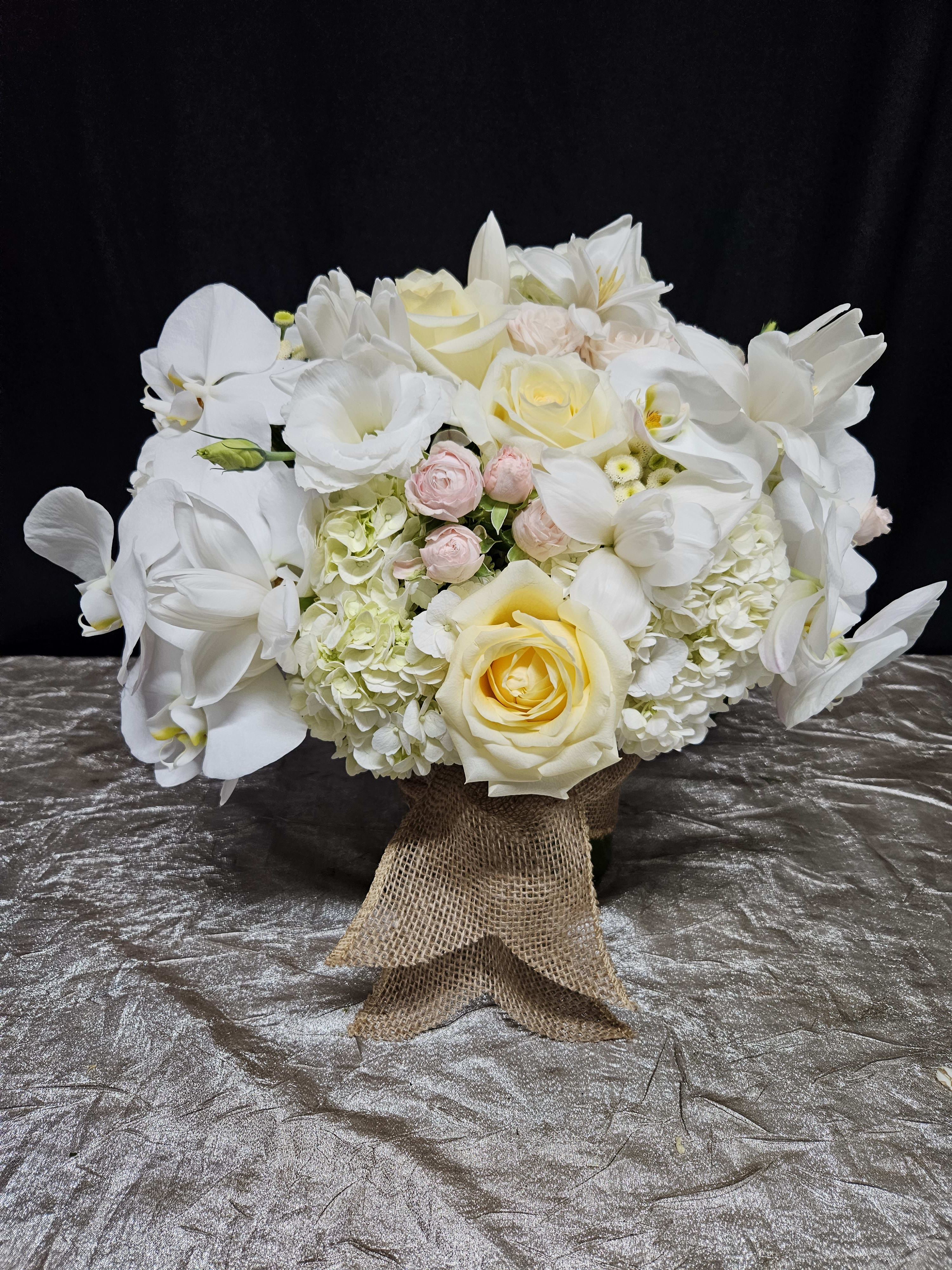 White floral bouquet with roses, orchids, and hydrangeas tied with burlap ribbon