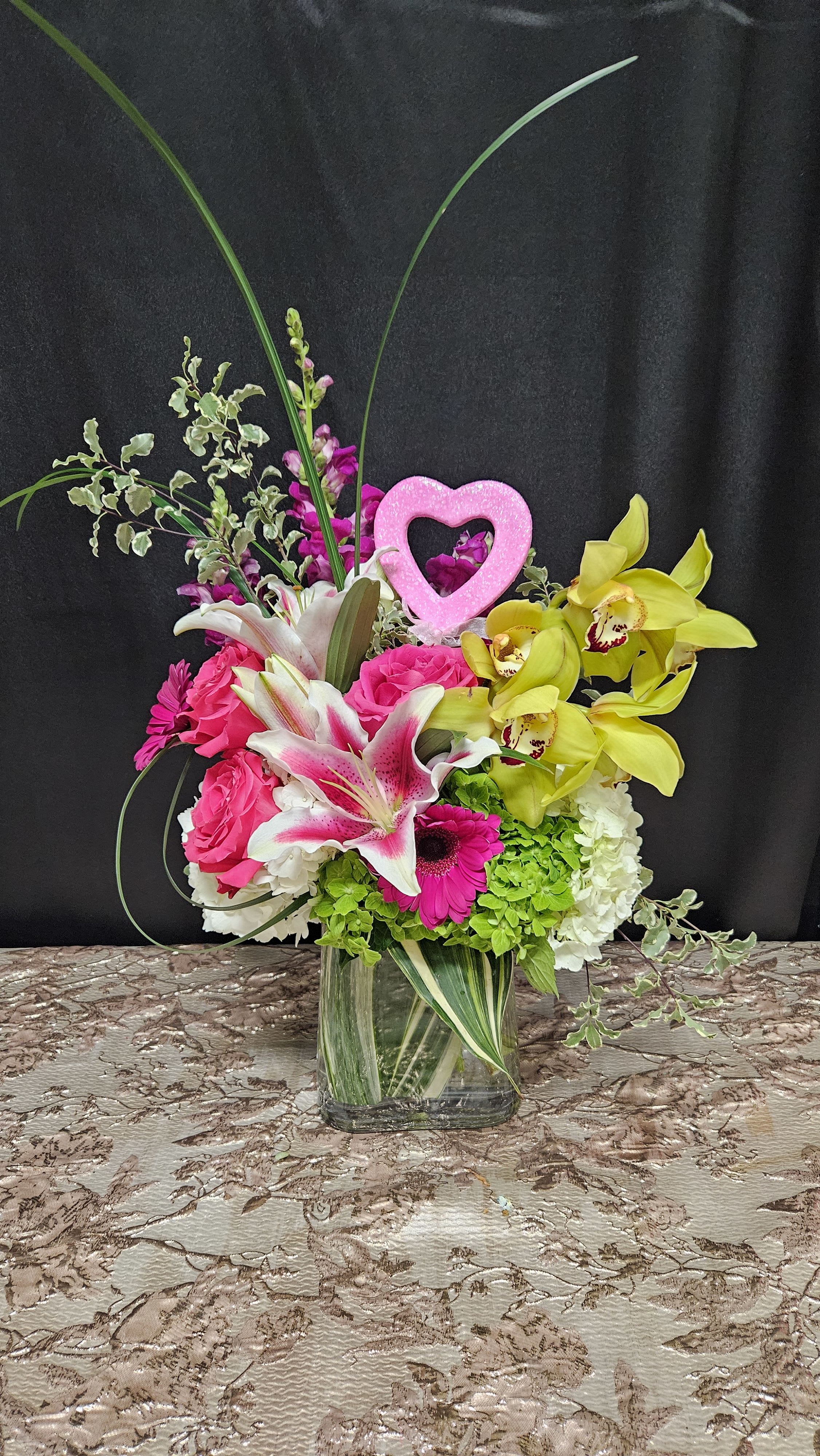 Bright mixed bouquet in a clear glass vase with a pink heart pick