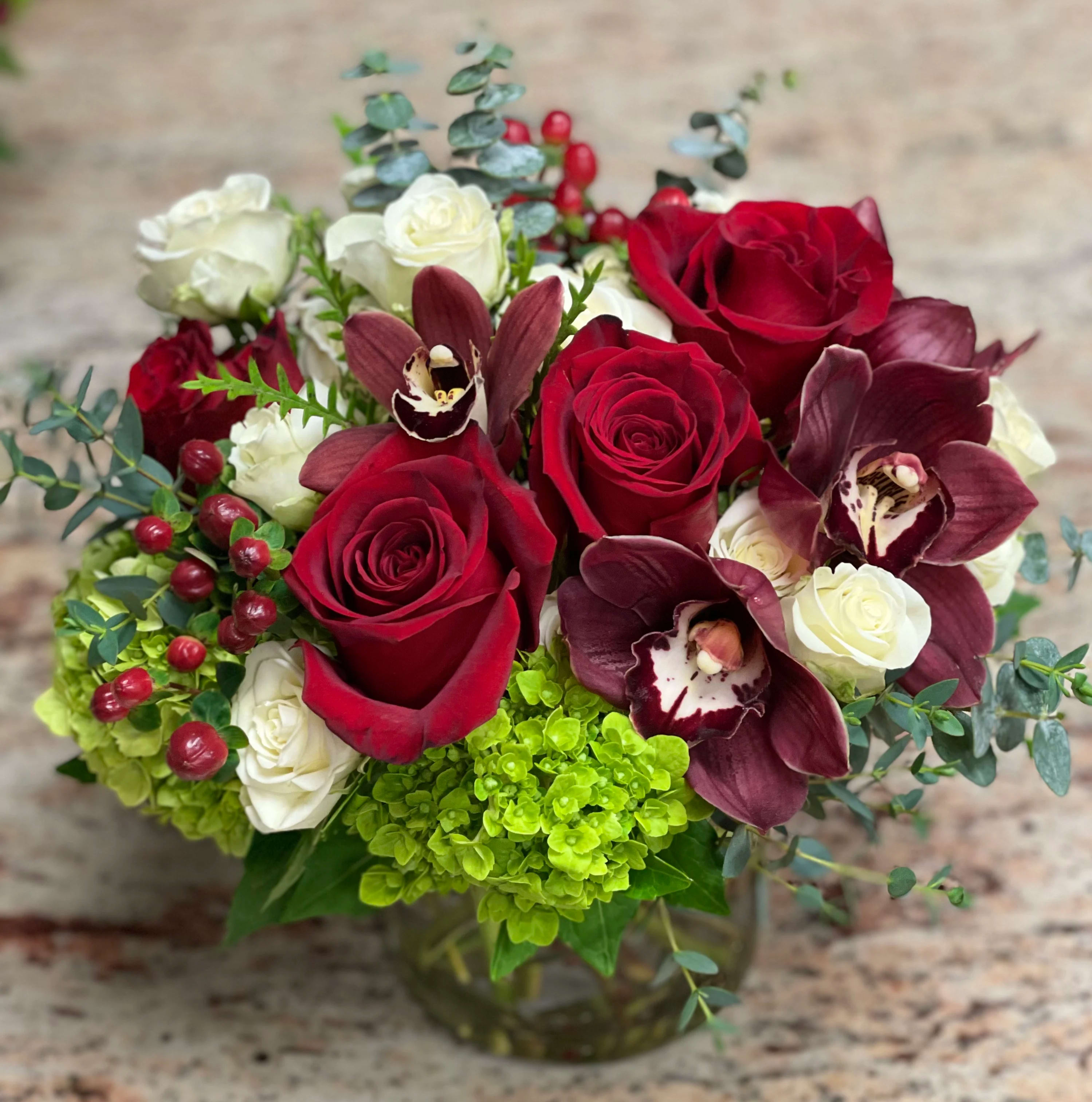 Red and white roses with burgundy orchids in a glass vase