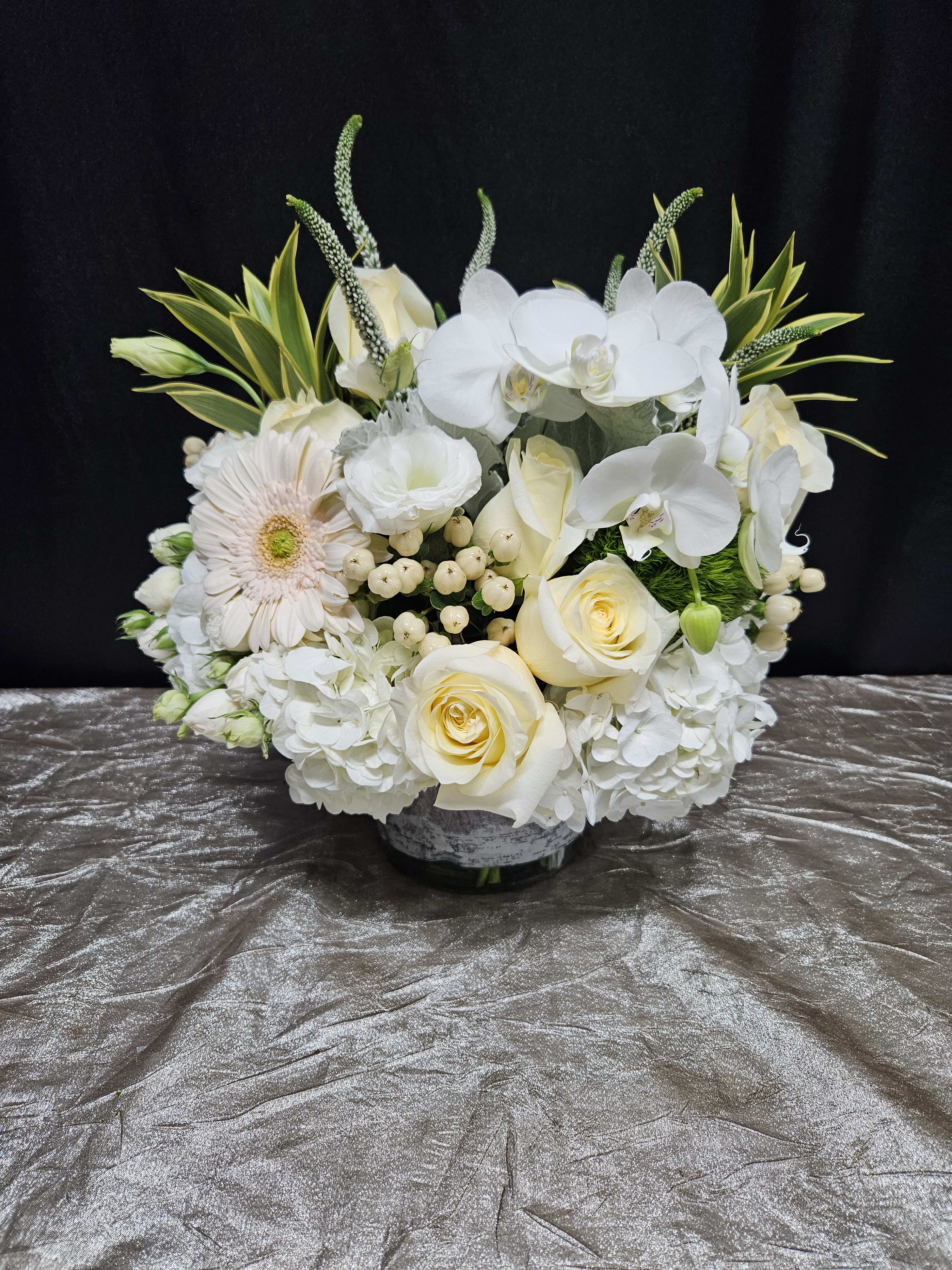 White floral arrangement with roses, orchids, and a gerbera daisy in a low vase