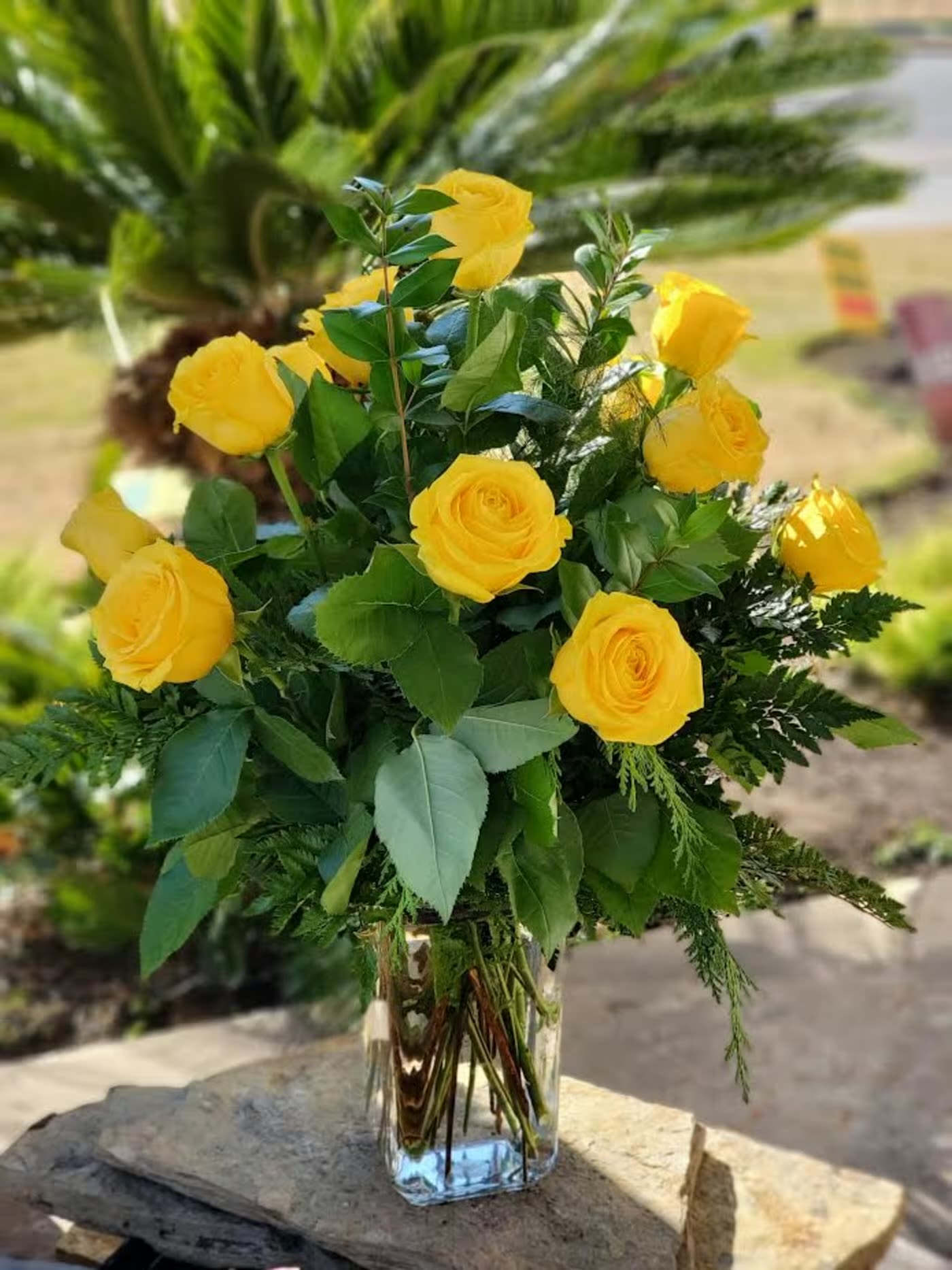 Tall arrangement of yellow roses with lush greenery in a clear glass vase