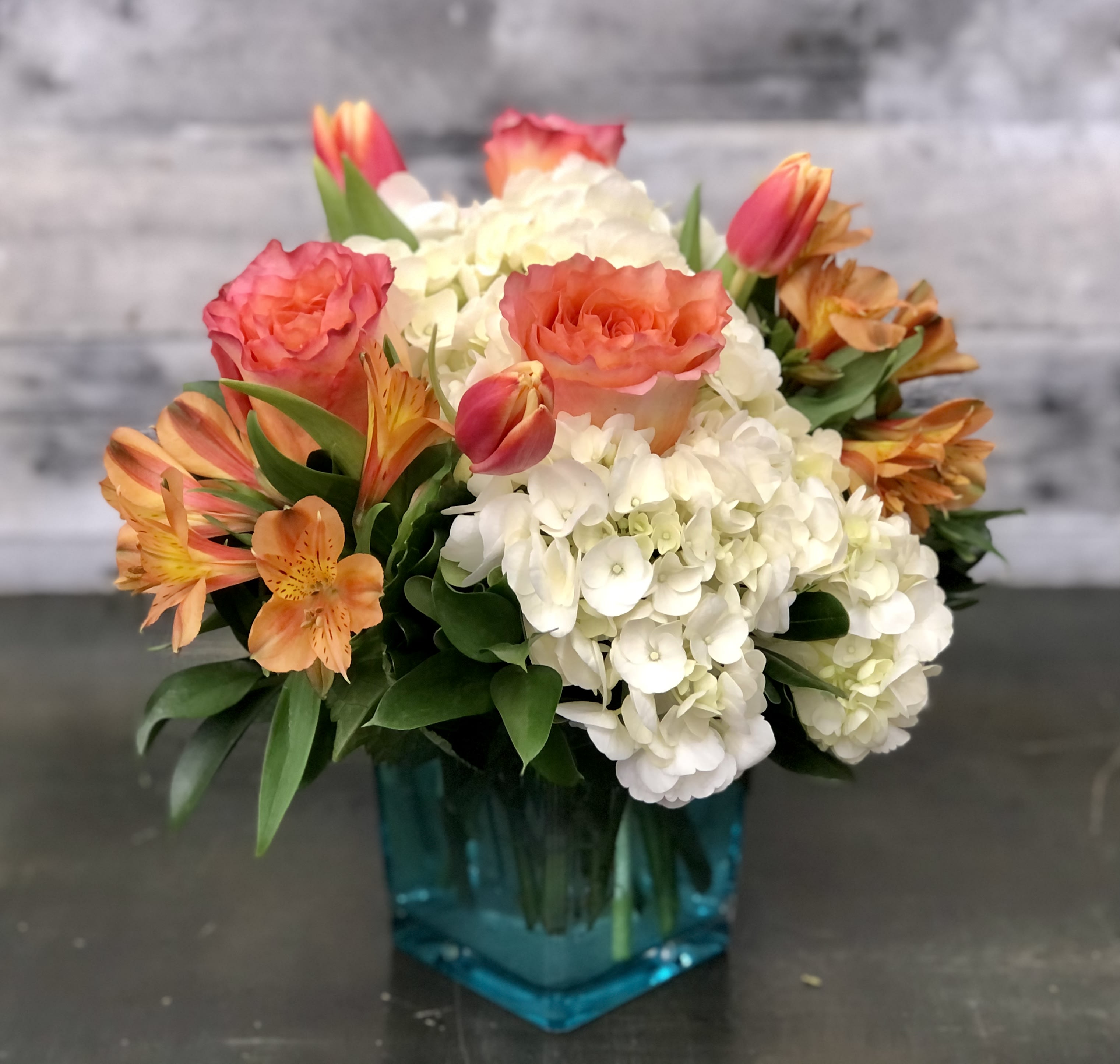 Bouquet of orange and pink roses with white hydrangeas in a blue vase