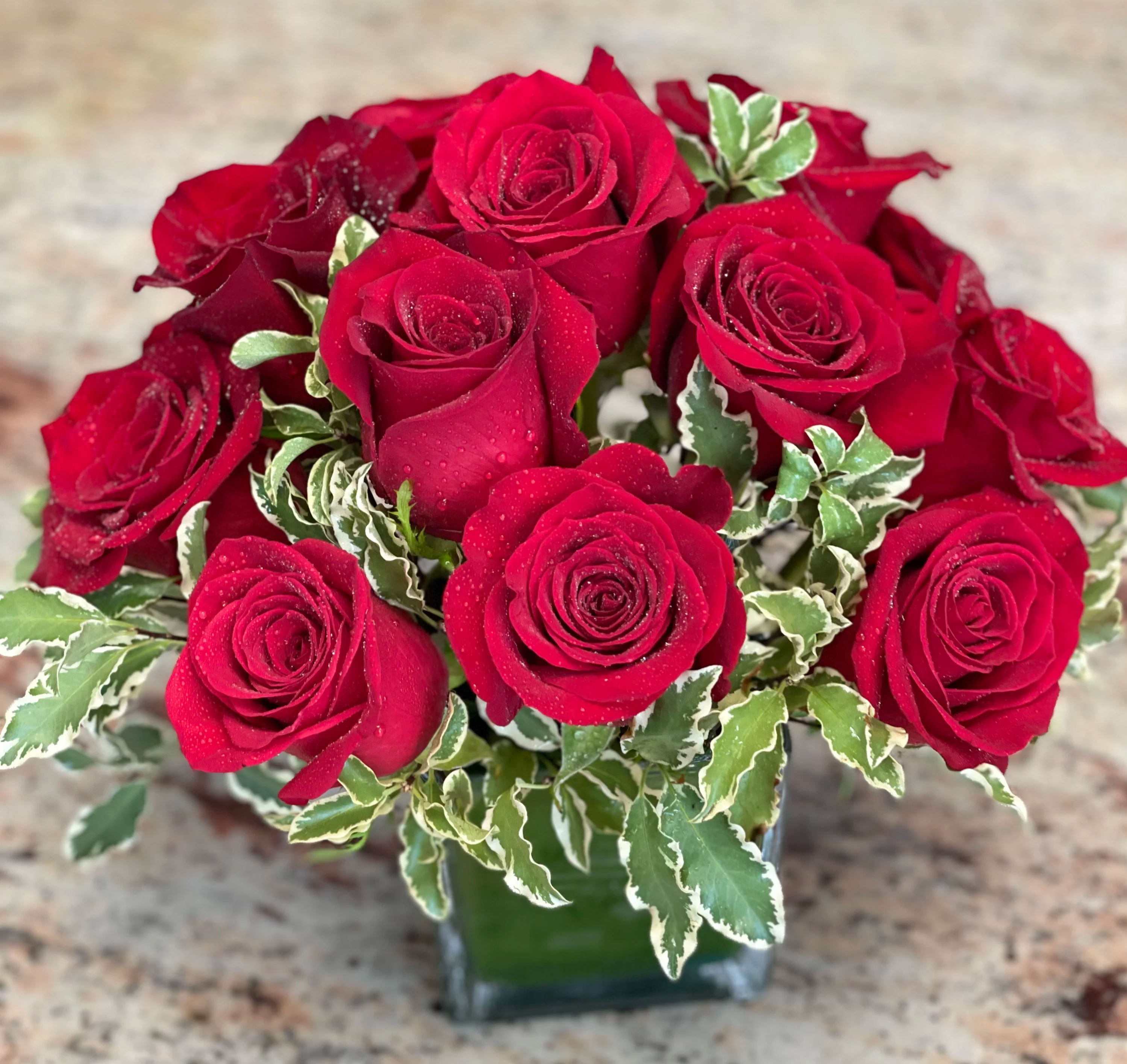 Red roses arranged in a clear glass vase with variegated greenery