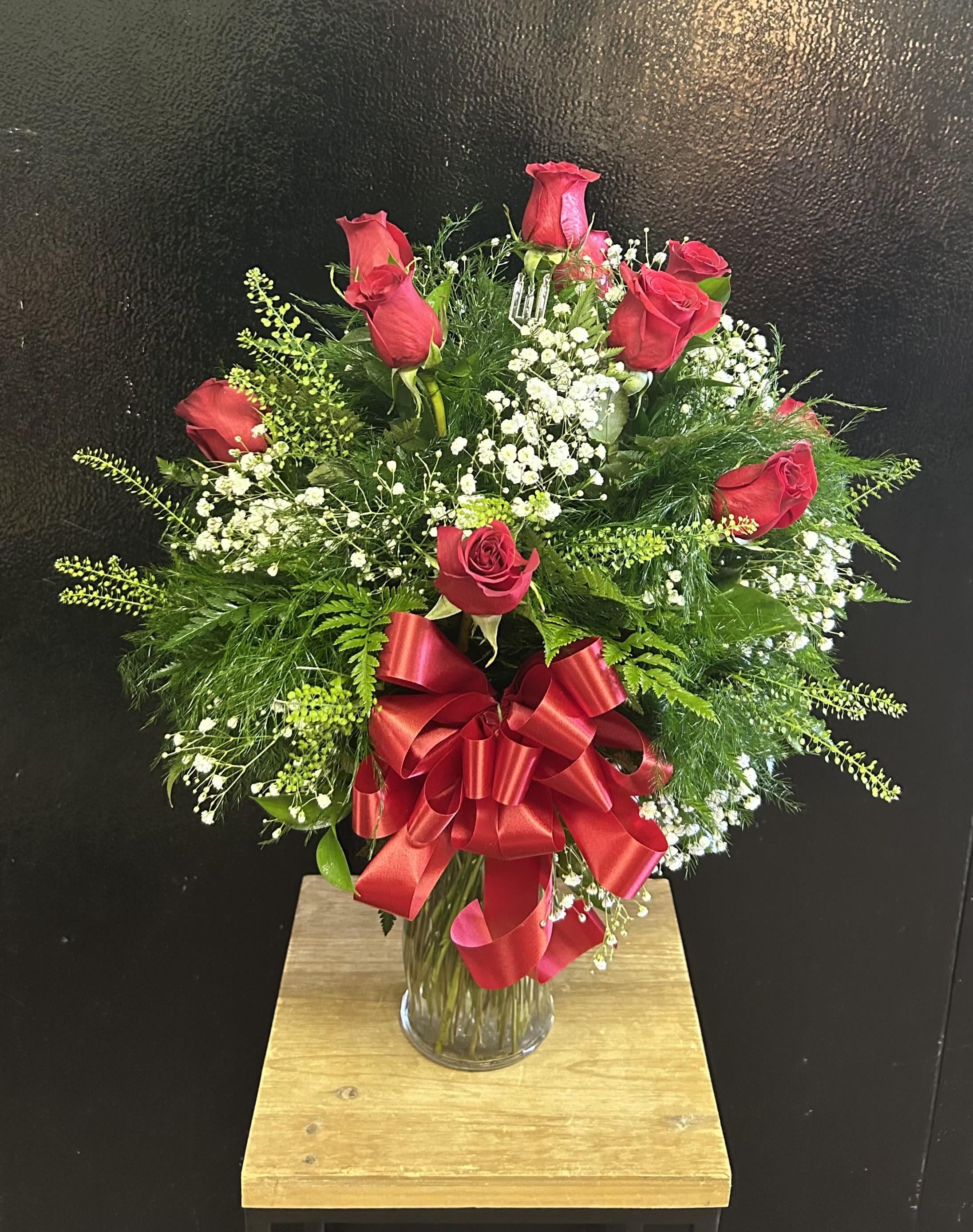 Red rose arrangement in a clear glass vase with a large red ribbon