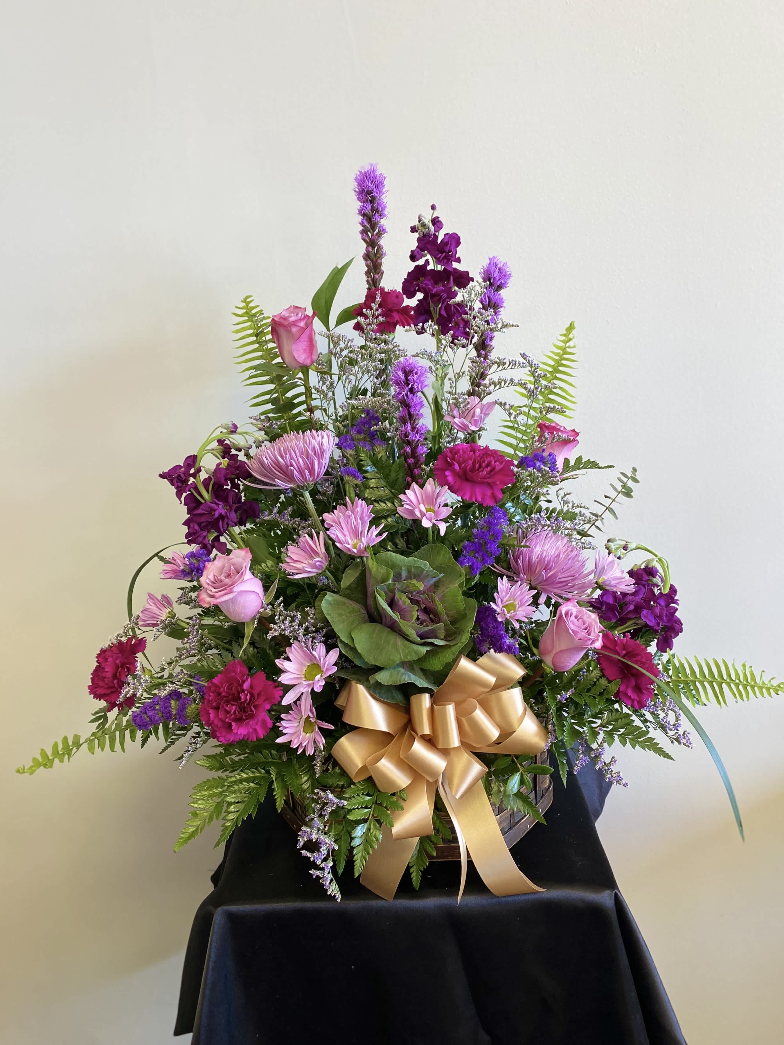 Pink and purple mixed flower arrangement with a gold ribbon in a basket