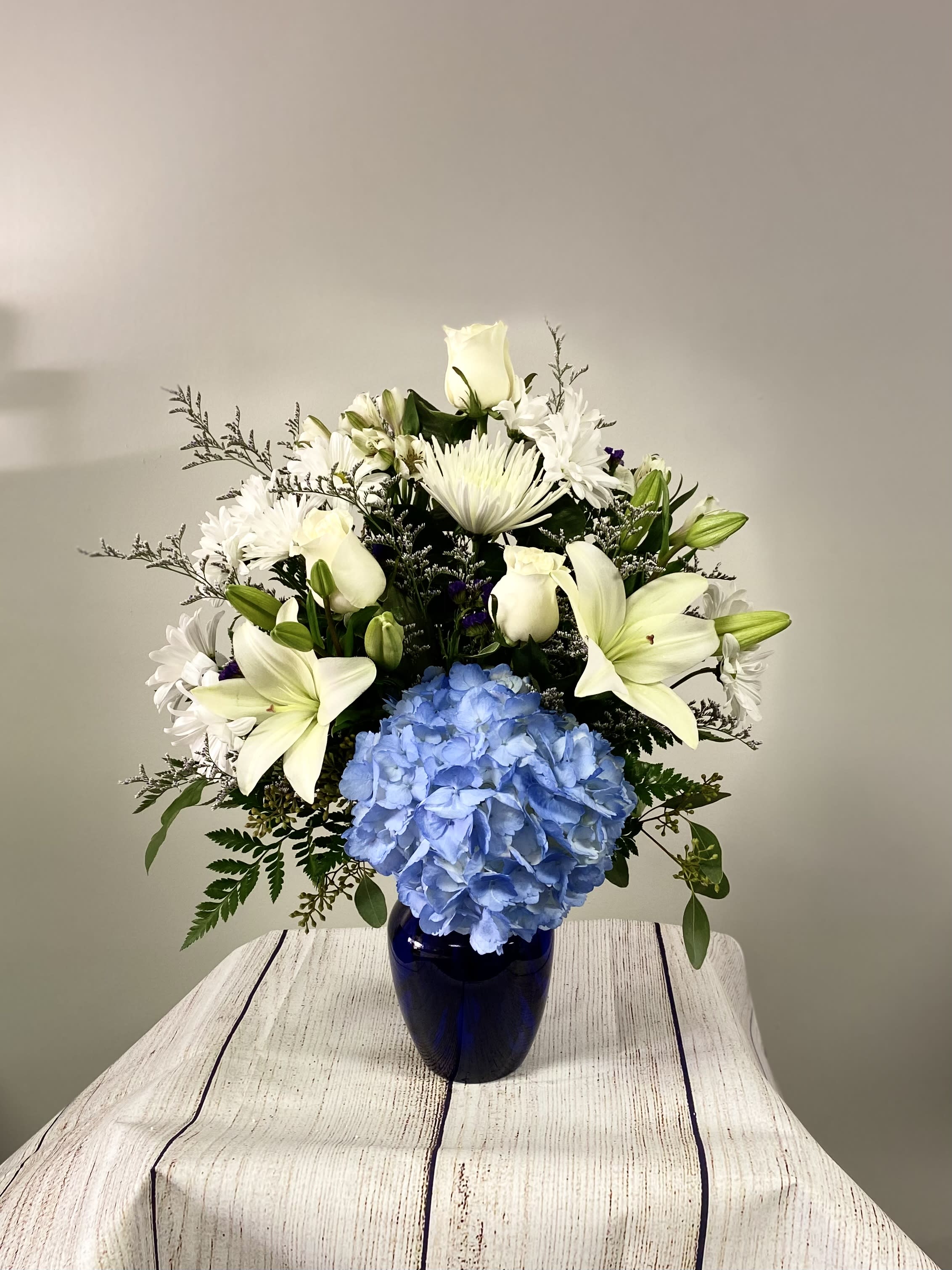 White lilies and daisies with a blue hydrangea in a dark vase