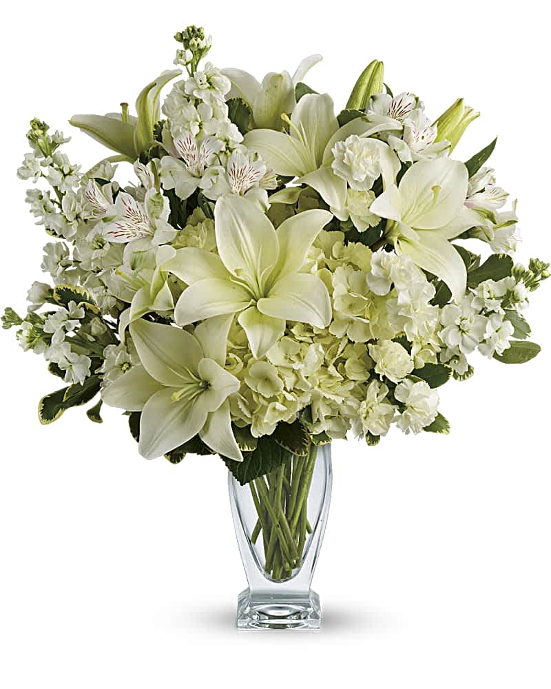 White lilies and mixed white flowers in a clear glass vase