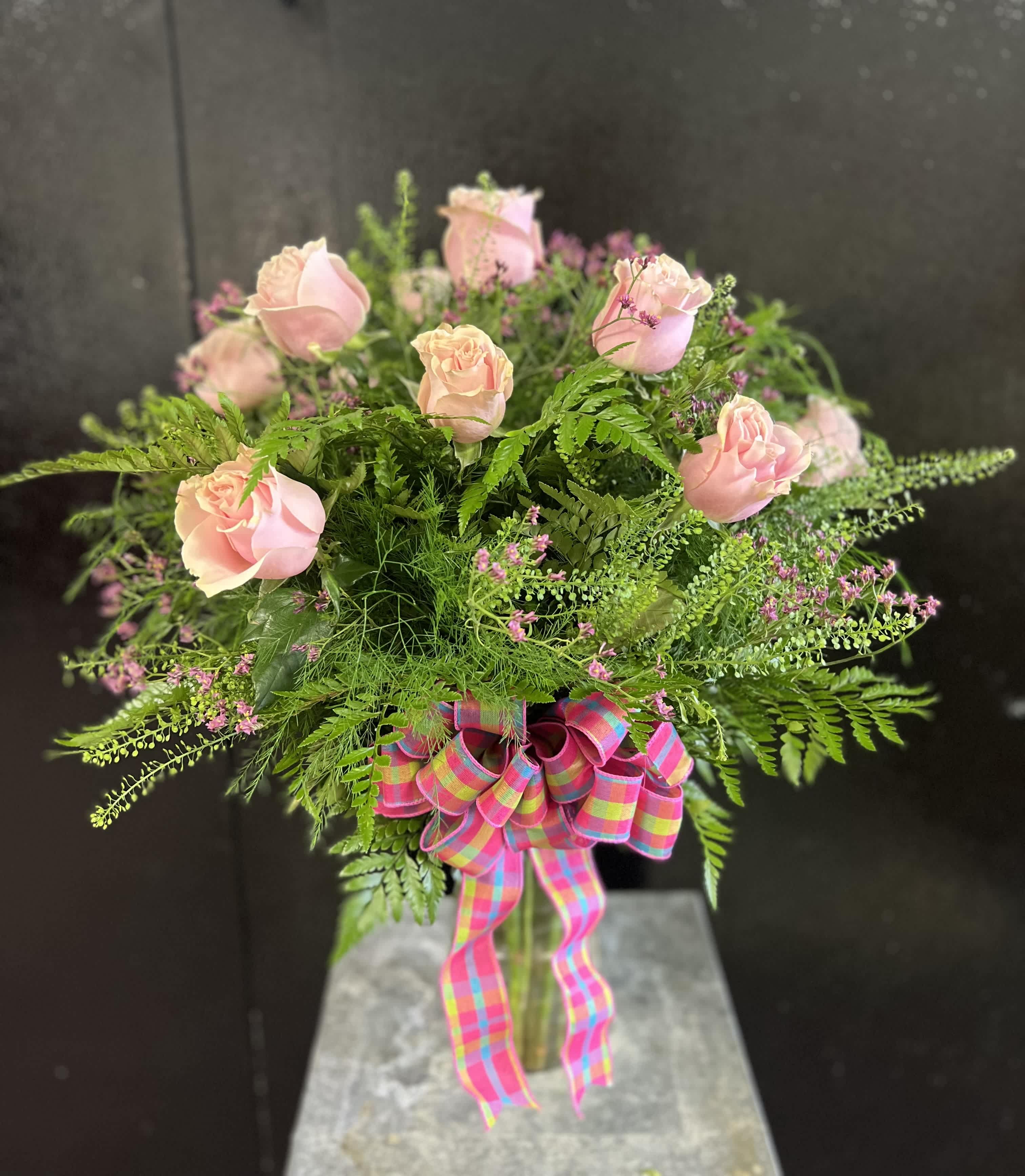 Pink roses in a glass vase with a colorful plaid ribbon