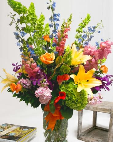 Tall mixed bouquet with lilies, roses, orchids, and blue flowers in a glass vase
