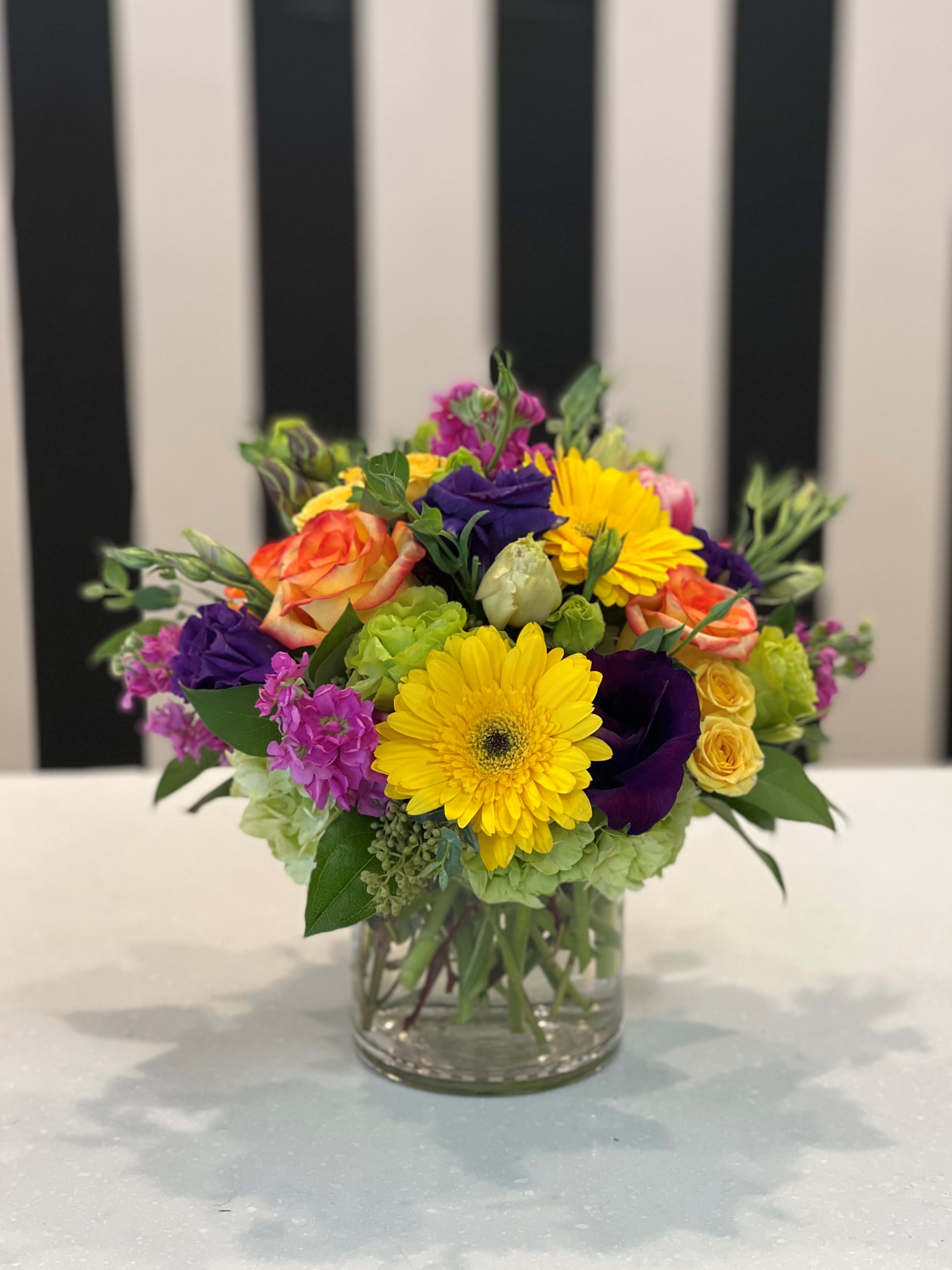 Mixed bouquet in a clear glass vase with yellow, purple, pink, and orange blooms