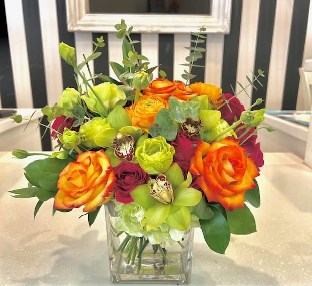Bright mixed bouquet of roses and green orchids in a clear glass vase