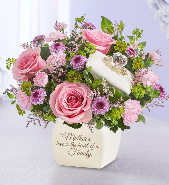 A Mother’s Love™  -  A mother’s love is the heart of every family. This sentiment is perfectly captured in our garden-inspired bouquet, featuring a mix of pastel blooms in our vintage-inspired canister. Crafted with an elegant glass heart accented by a gold filigree collar, this timeless keepsake is a lasting reminder of the special bond you share.      All-around arrangement with light pink roses and mini carnations, pink limonium and lavender button poms; accented with assorted greenery     Artistically designed in our exclusive gift canister, crafted with an elegant glass heart and accented by a gold filigree collar on a ceramic base; features the heartfelt message: “A Mother’s love is the Heart of a Family;” can later be used to hold jewelry/trinkets; measures 4.5"H      Arrangement measures approximately 10"H x 10"W        Our florists hand-design each arrangement, so colors and varieties may vary due to local availability
