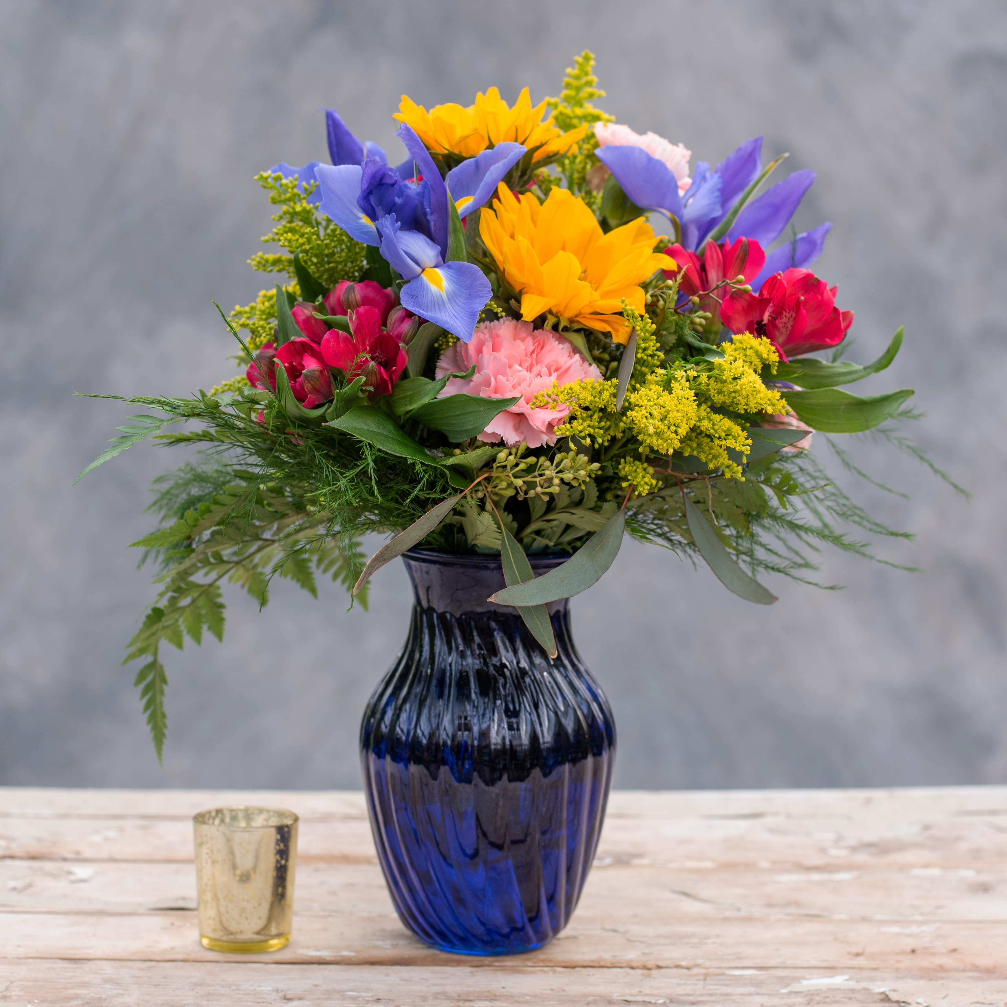 Colorful mixed bouquet in a blue glass vase with a small candle beside it