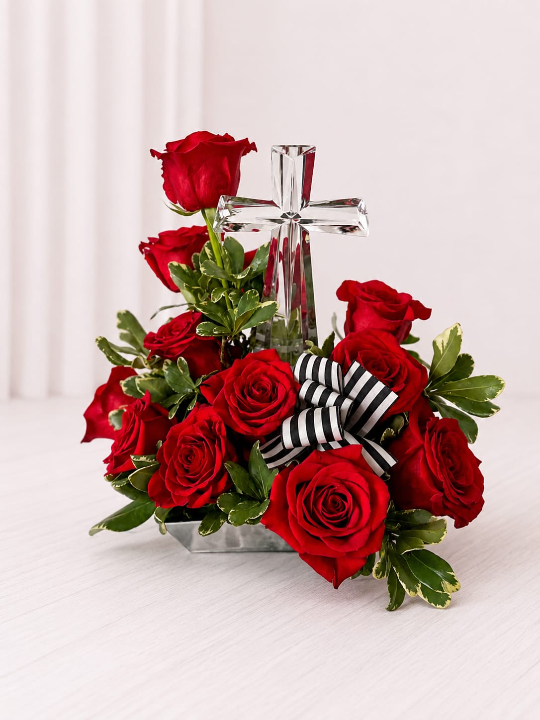 Red roses arranged around a clear glass cross with a striped ribbon