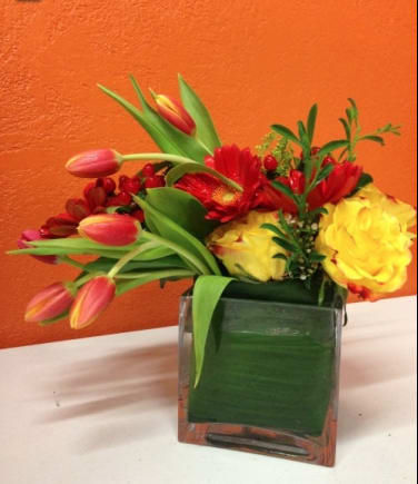 Colorful bouquet of tulips, roses, and gerbera daisies in a square glass vase