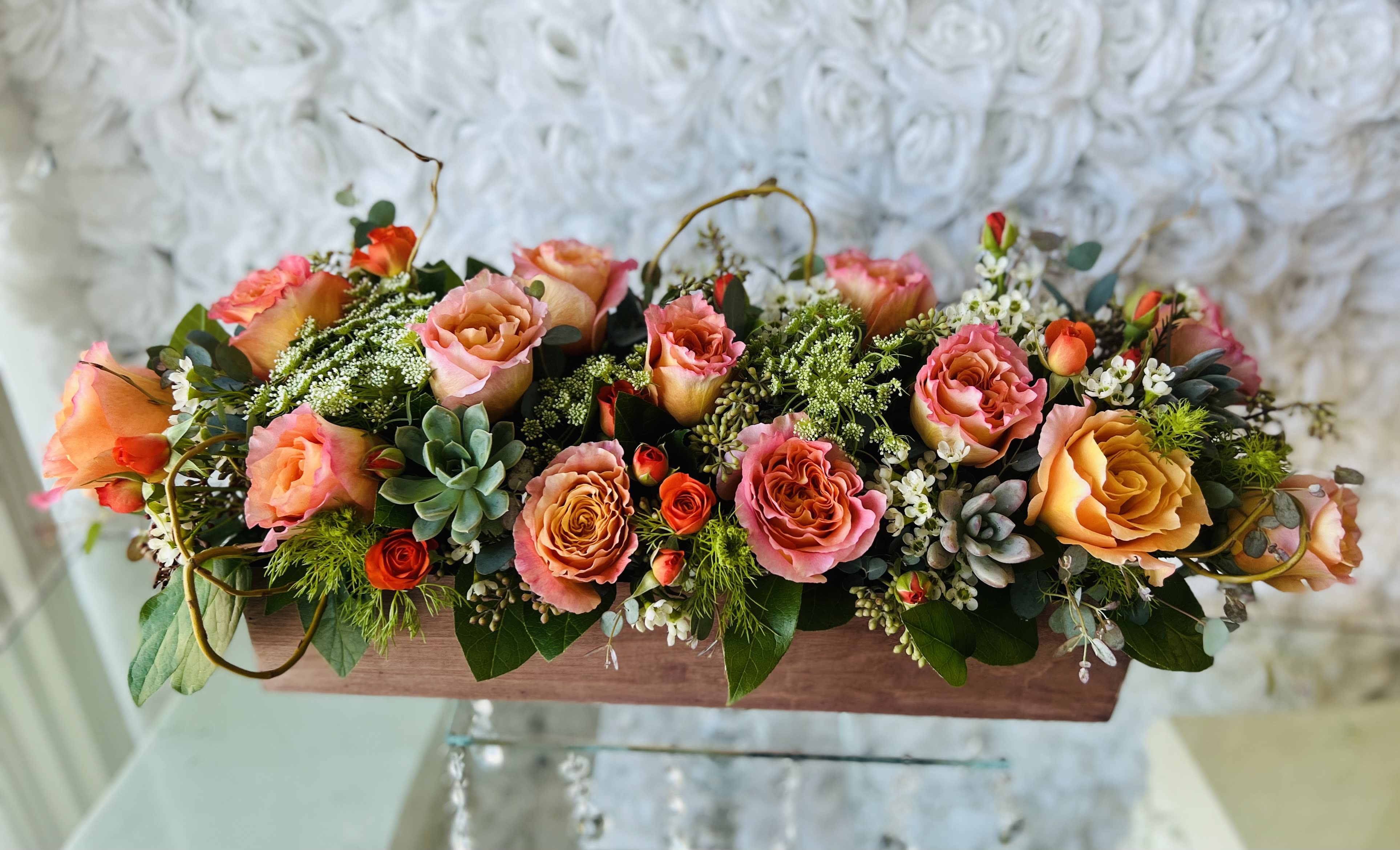 Long low floral arrangement with pink and orange roses in a wooden box
